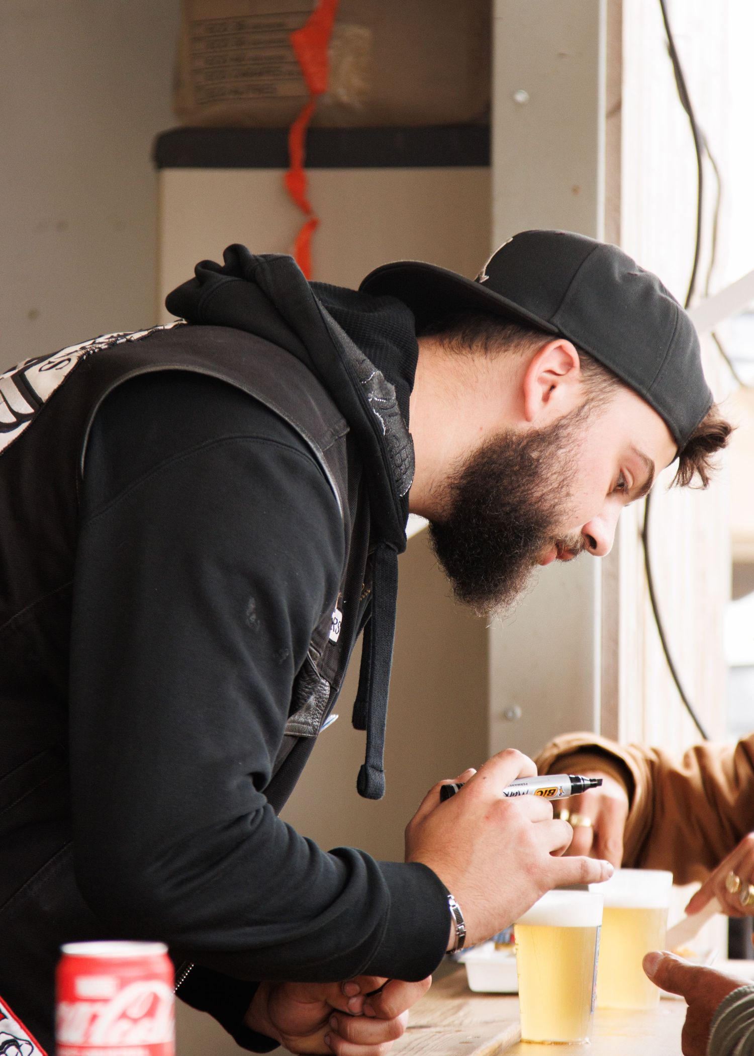 Person in black hoodie and cap looking down at mobile phone indoors.
