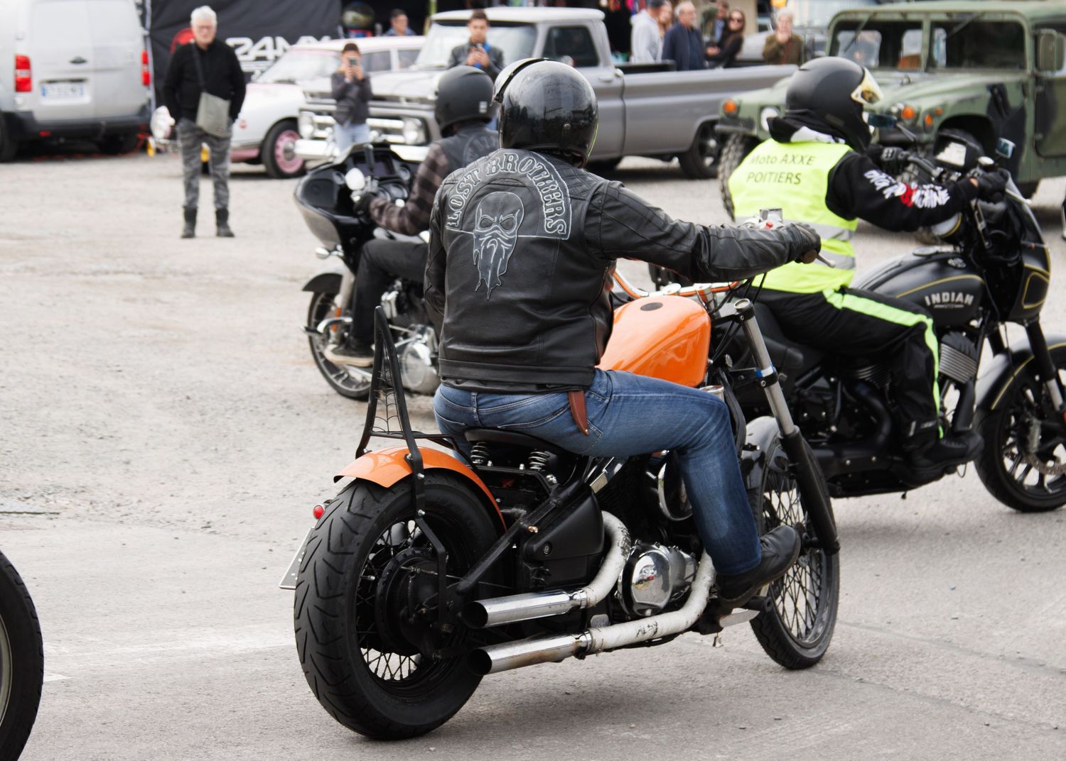 Motorcyclist in black leather jacket riding customized bike in parking area.