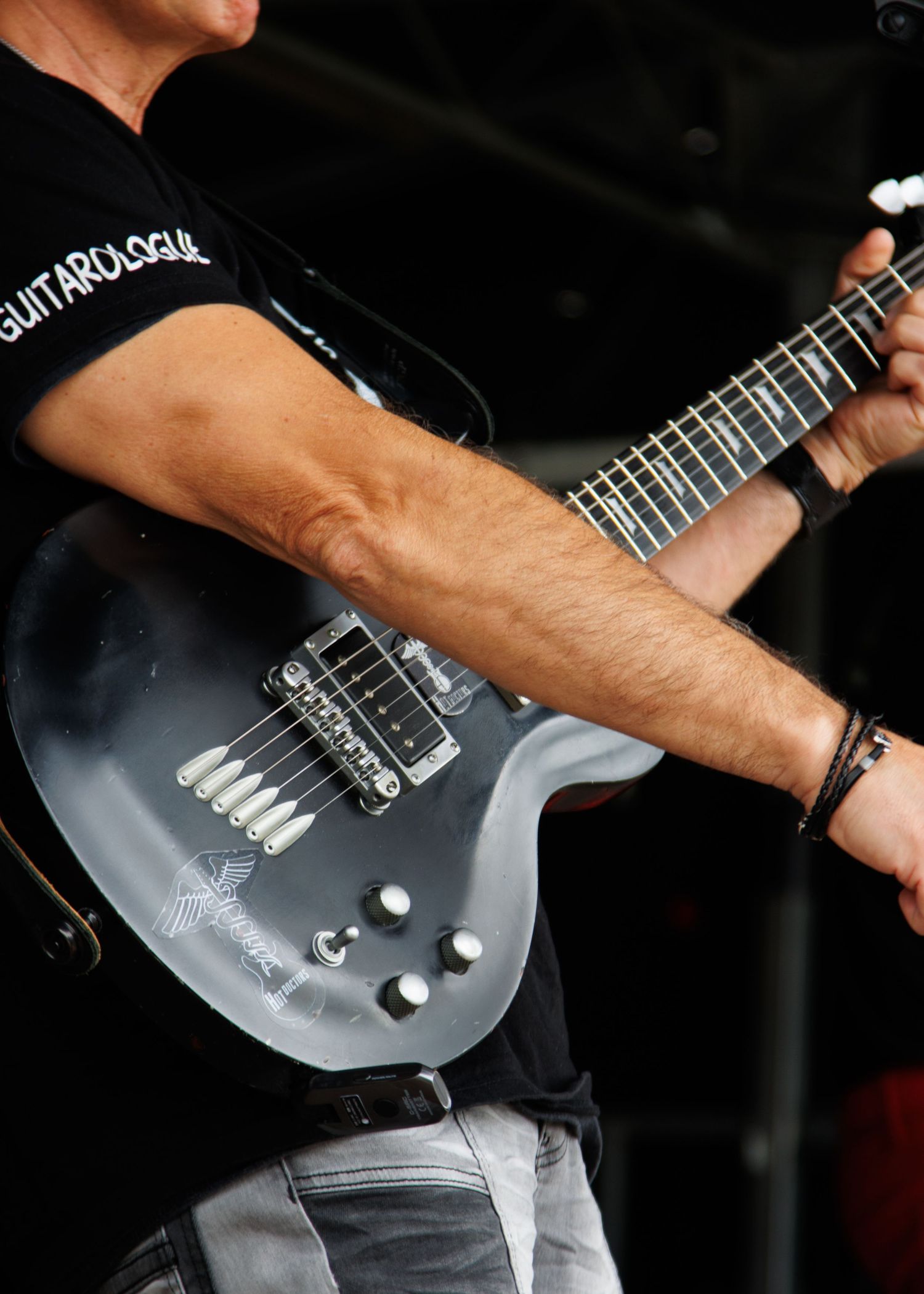 Close-up of hands playing a black electric guitar on stage.