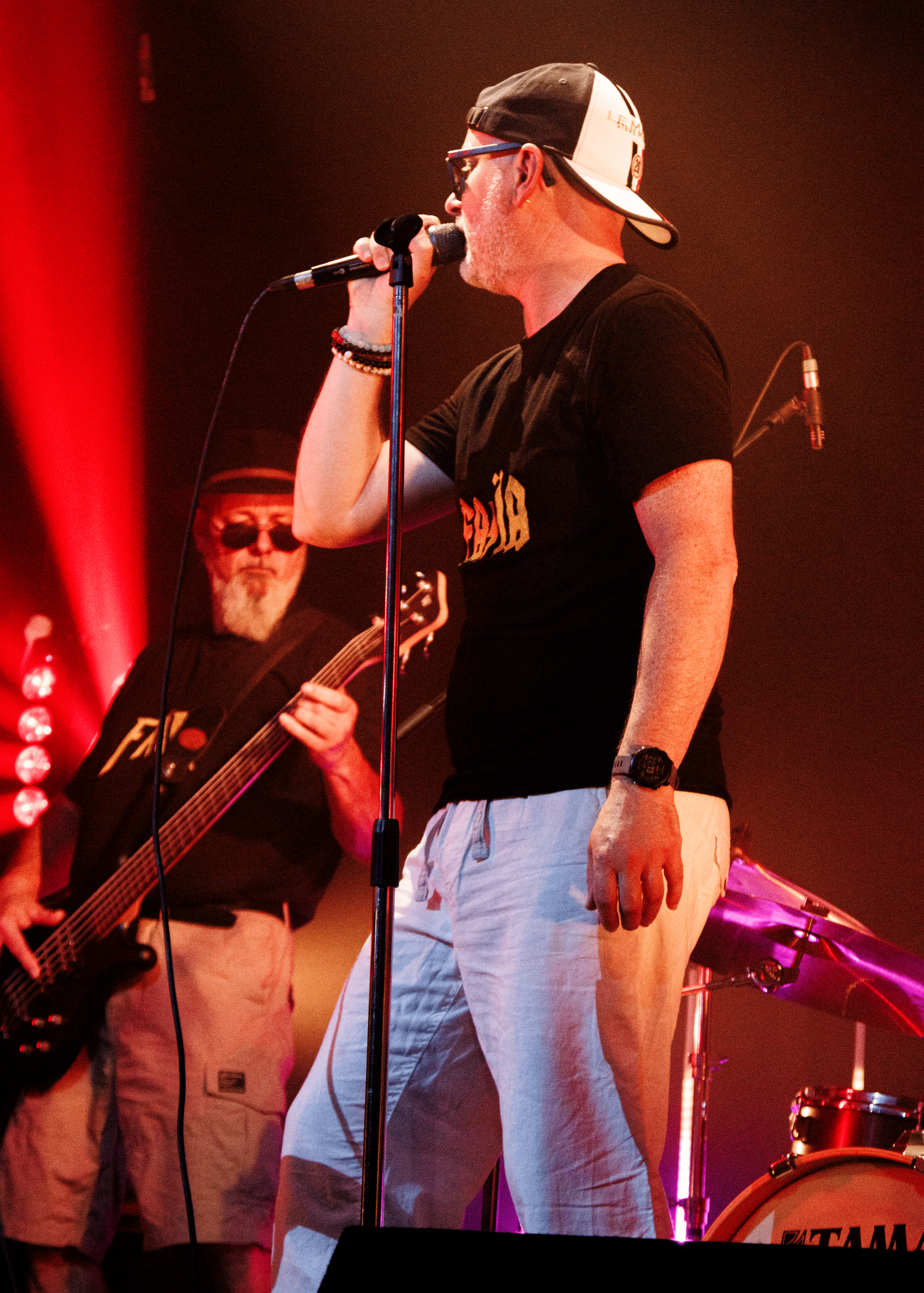 A singer performs with a band on stage, wearing casual attire under dramatic red concert lighting.