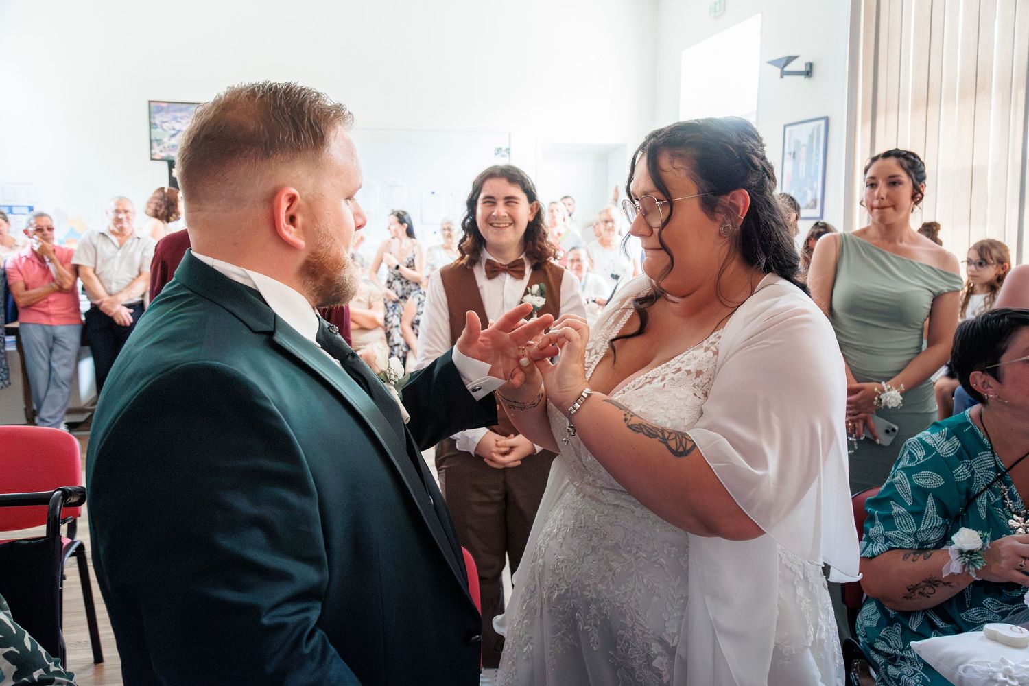 Bride and groom exchange rings during intimate indoor wedding ceremony with guests.