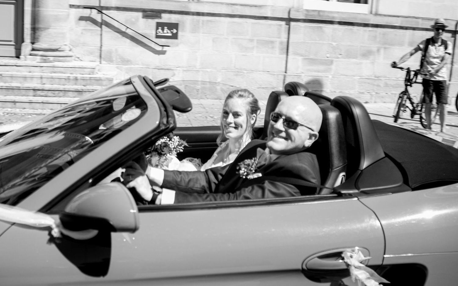 Bride and groom smile in a classic convertible car on their wedding day.