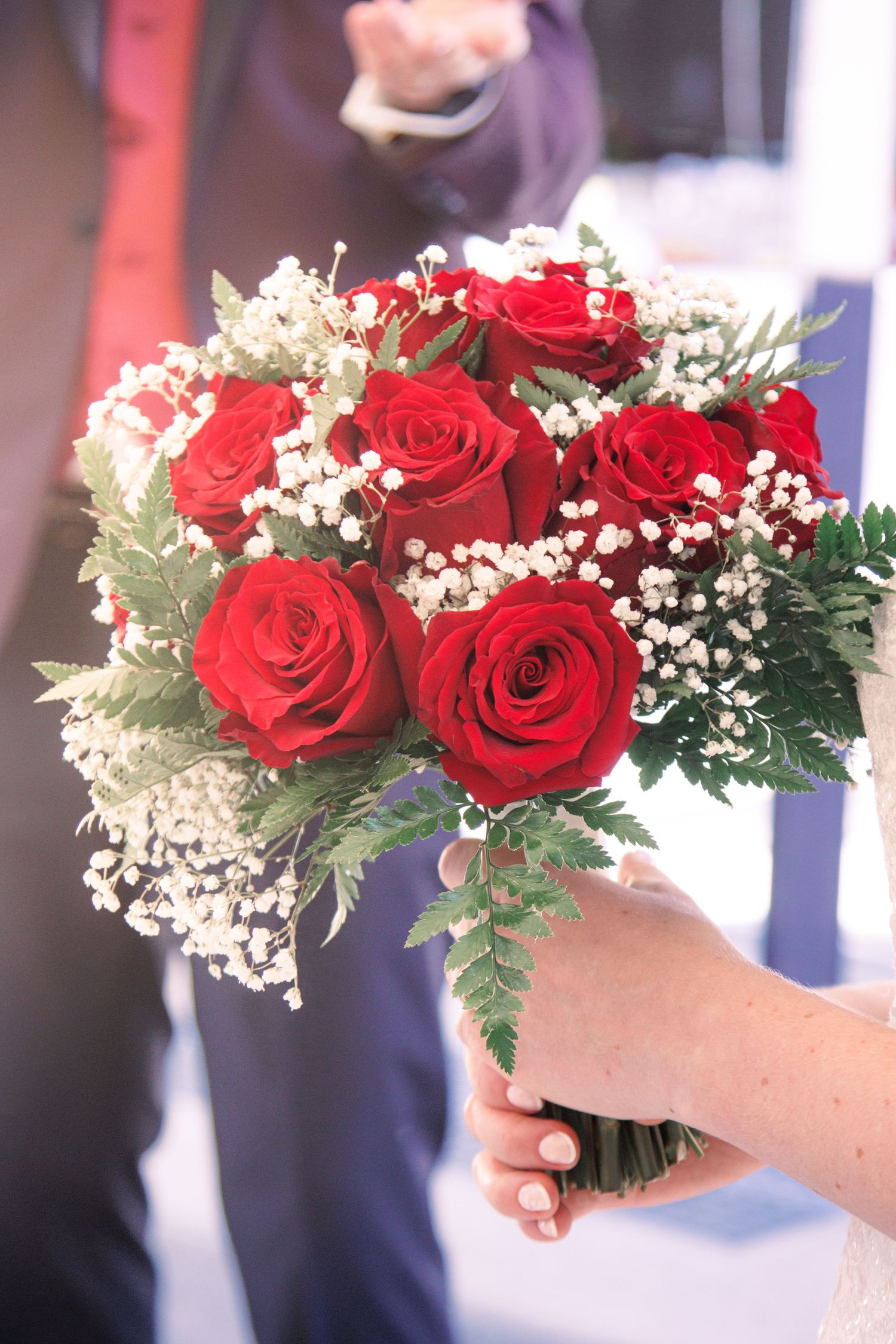 Close-up of bridal bouquet featuring red roses and white baby's breath flowers held by bride.