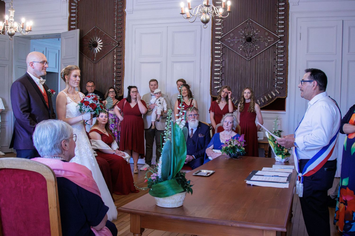 Officiant addresses bride, groom, and bridesmaids in burgundy during formal wedding ceremony.