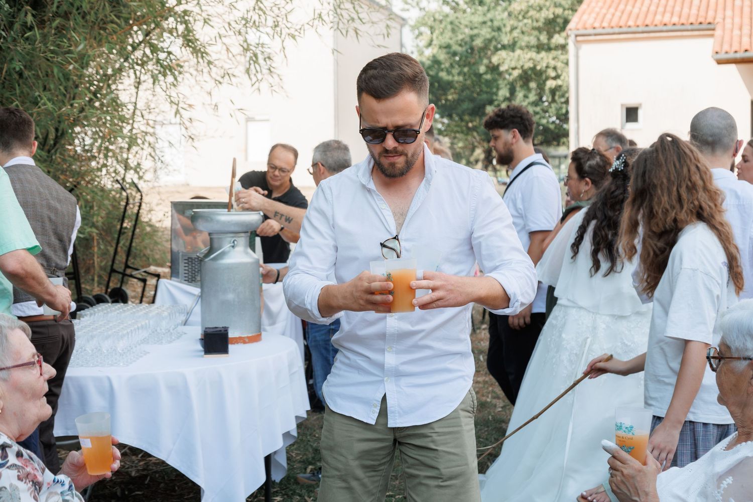 Man in white shirt pours drinks at outdoor wedding reception cocktail hour.