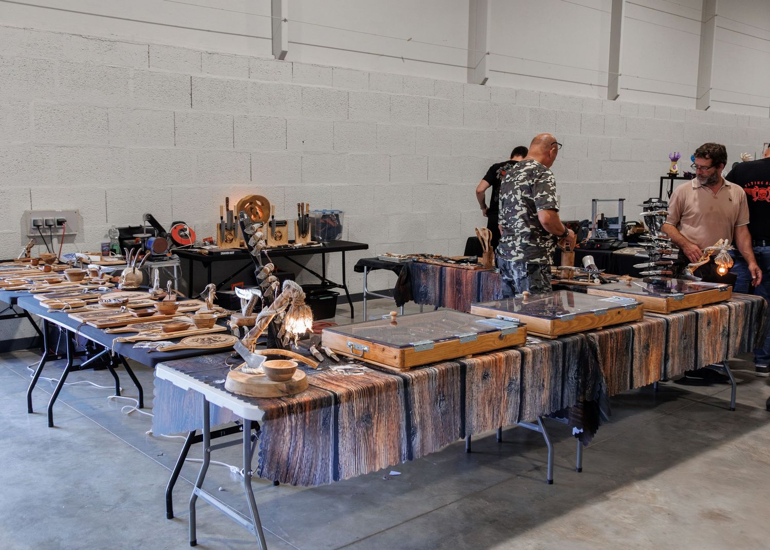 Craft fair display tables covered with handmade wooden items and decorative pieces in a large indoor venue.