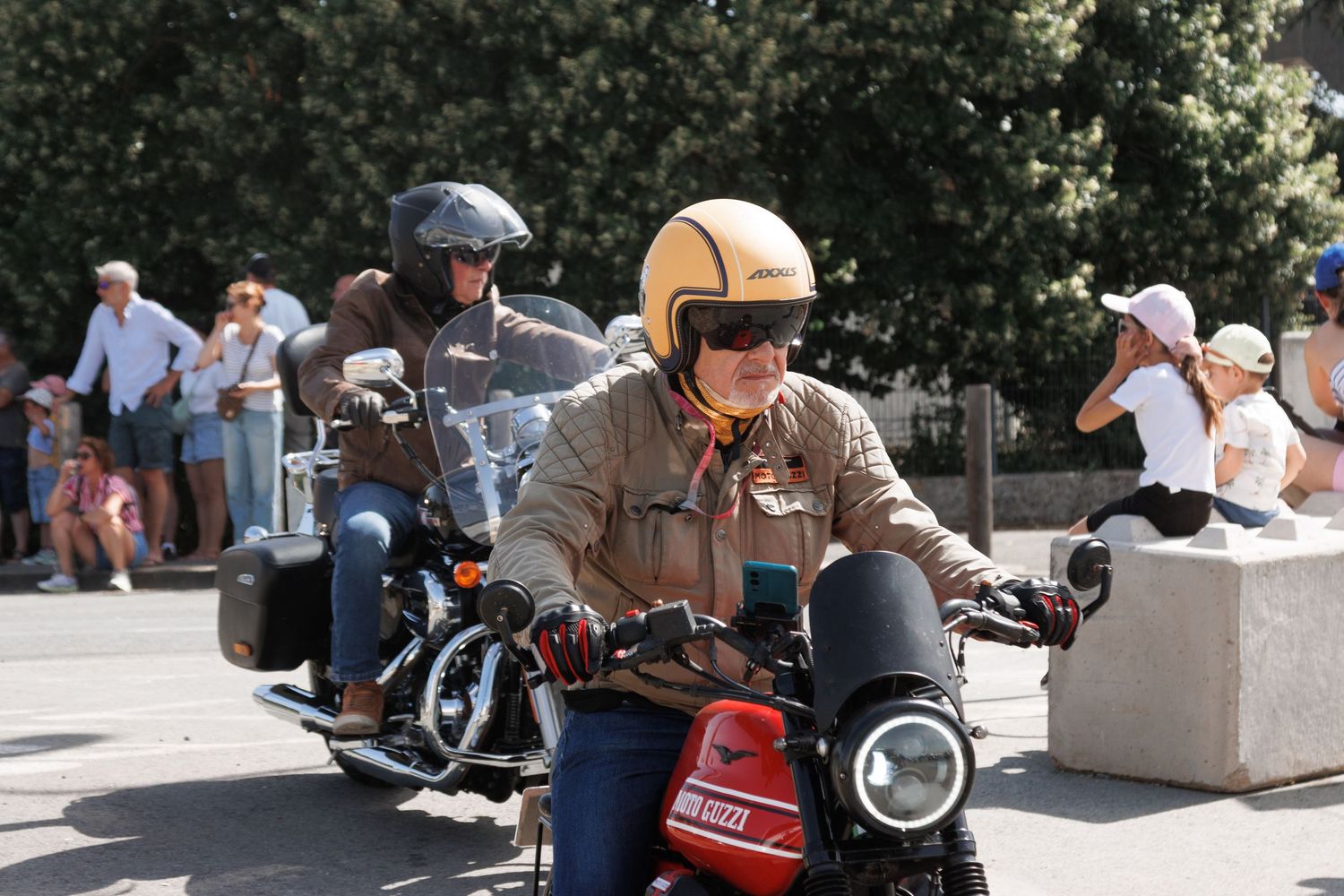 Motorcyclists riding Yamaha bikes in a sunny outdoor parade, with a rider in a tan jacket and gold helmet in the foreground.