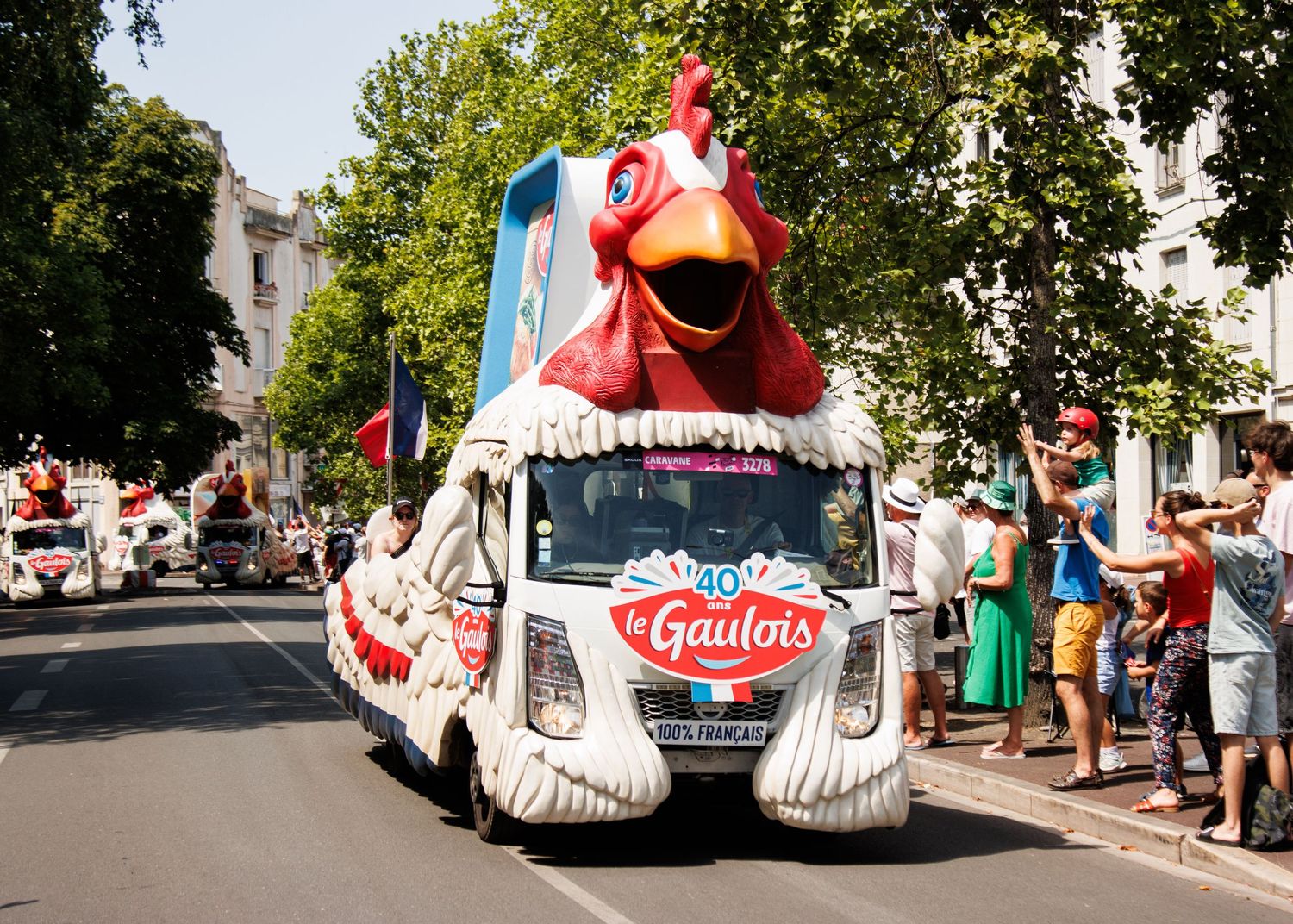 A promotional vehicle decorated as a giant red and white rooster drives through city streets.