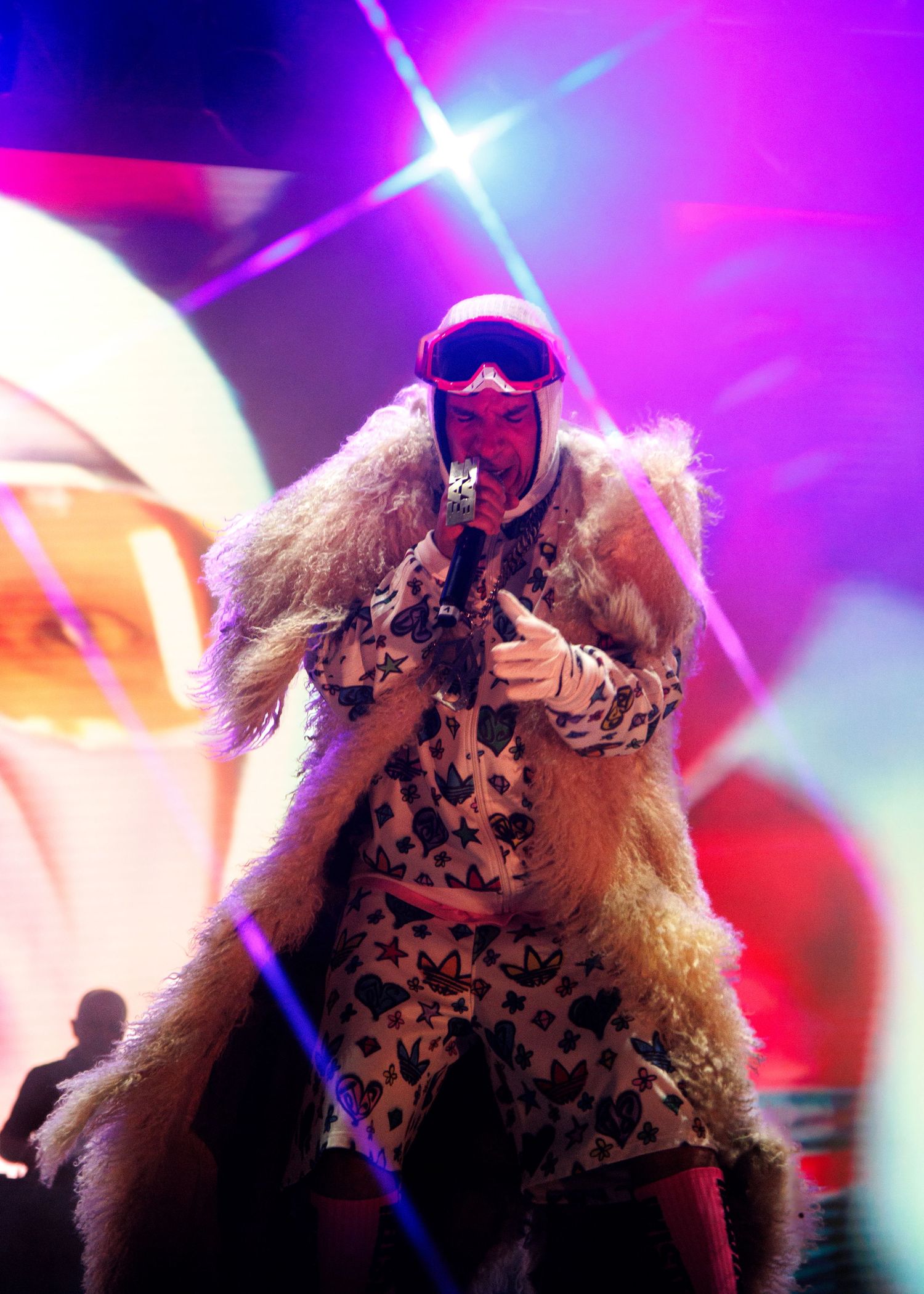 Energetic performer with flowing blonde hair and sunglasses illuminated by colorful stage lights during musical performance.