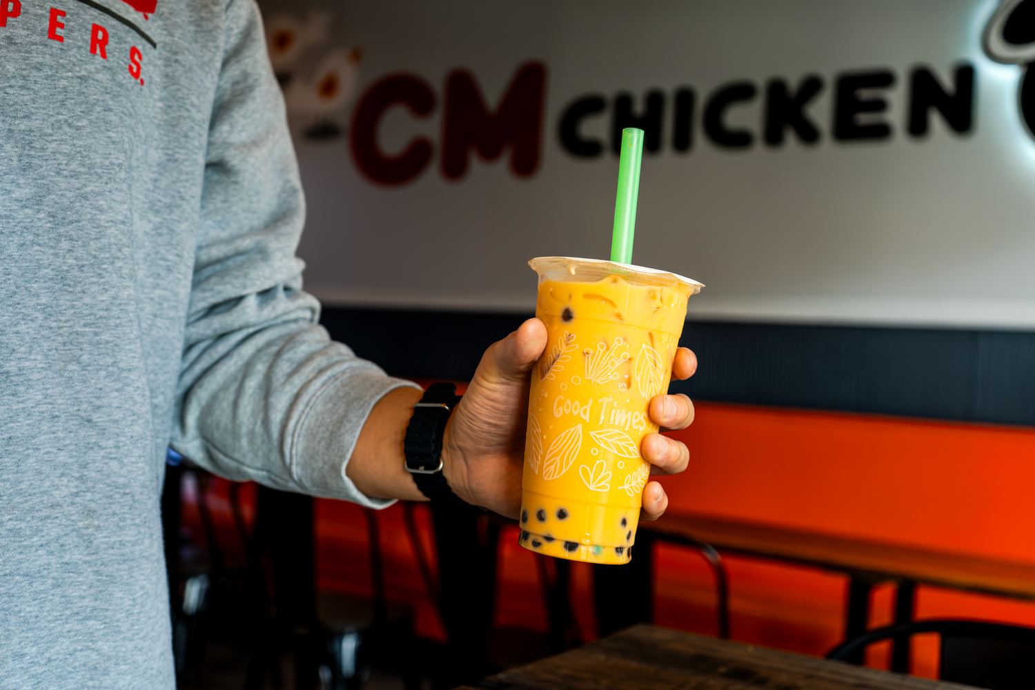 Person holding a bright yellow bubble tea drink with orange boba pearls against a dark background.