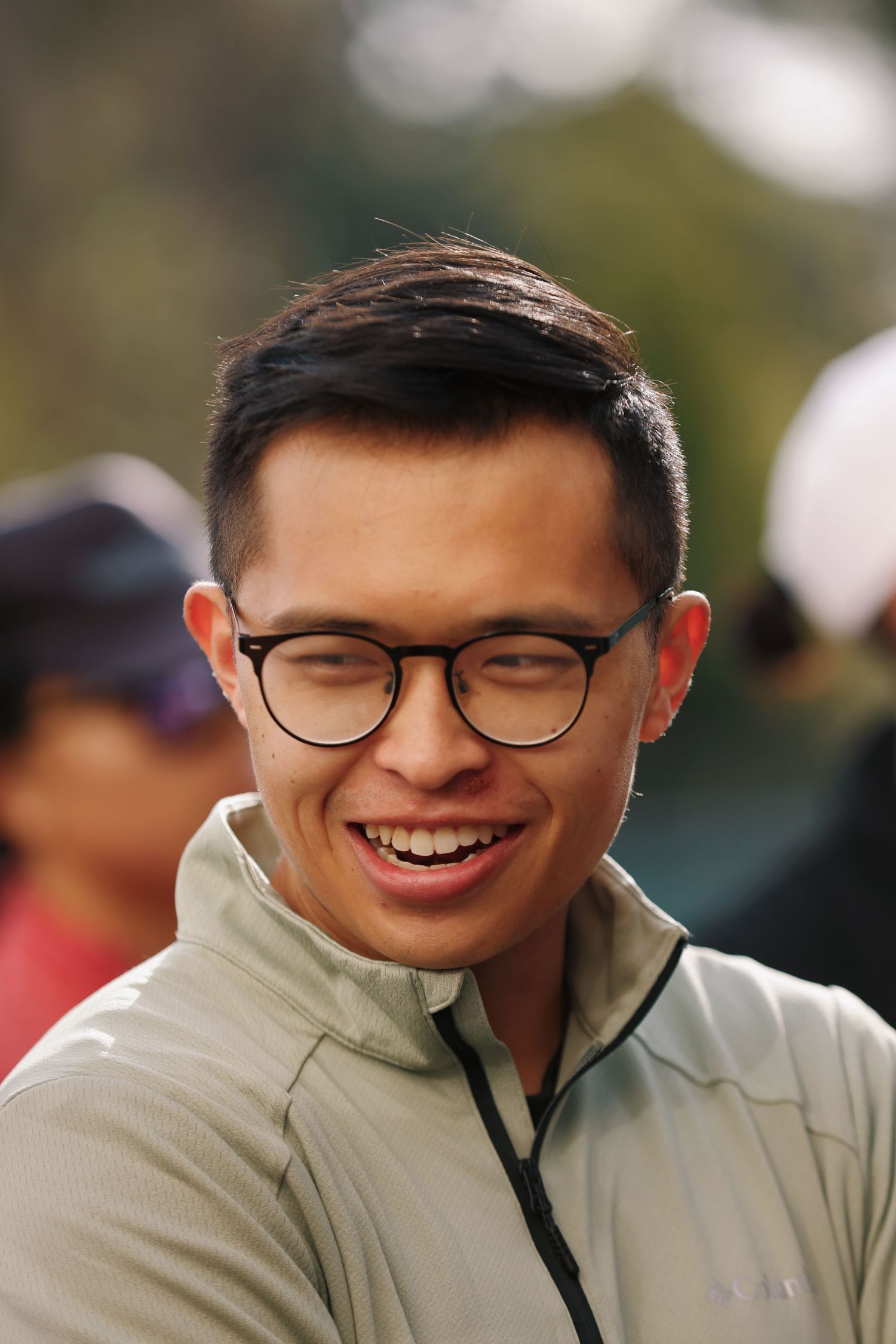 Casual portrait of someone in glasses and light jacket smiling warmly outdoors.