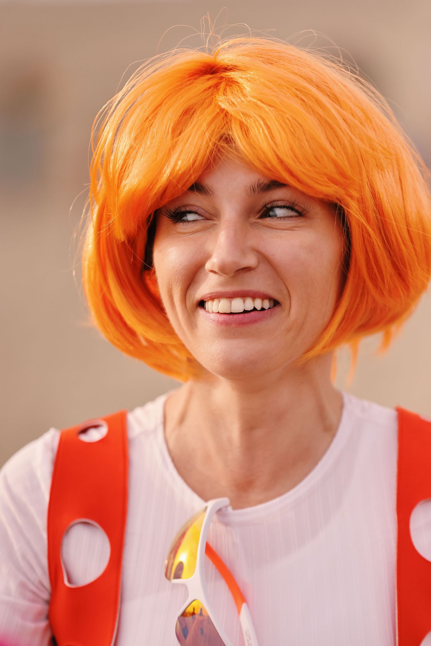 Portrait of someone wearing vibrant orange bob wig and polka dot outfit while smiling.