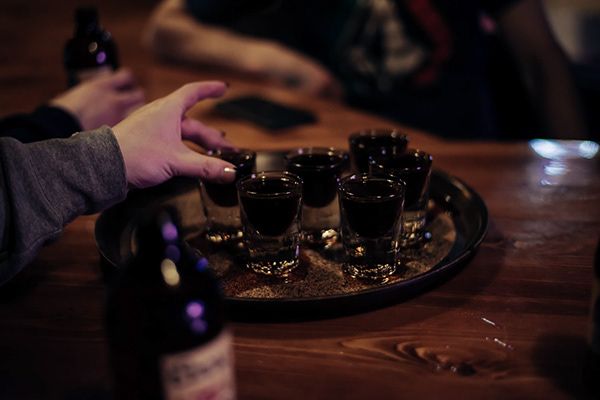 Dark moody shot of hands serving shots on a wooden tray in a dimly lit bar.