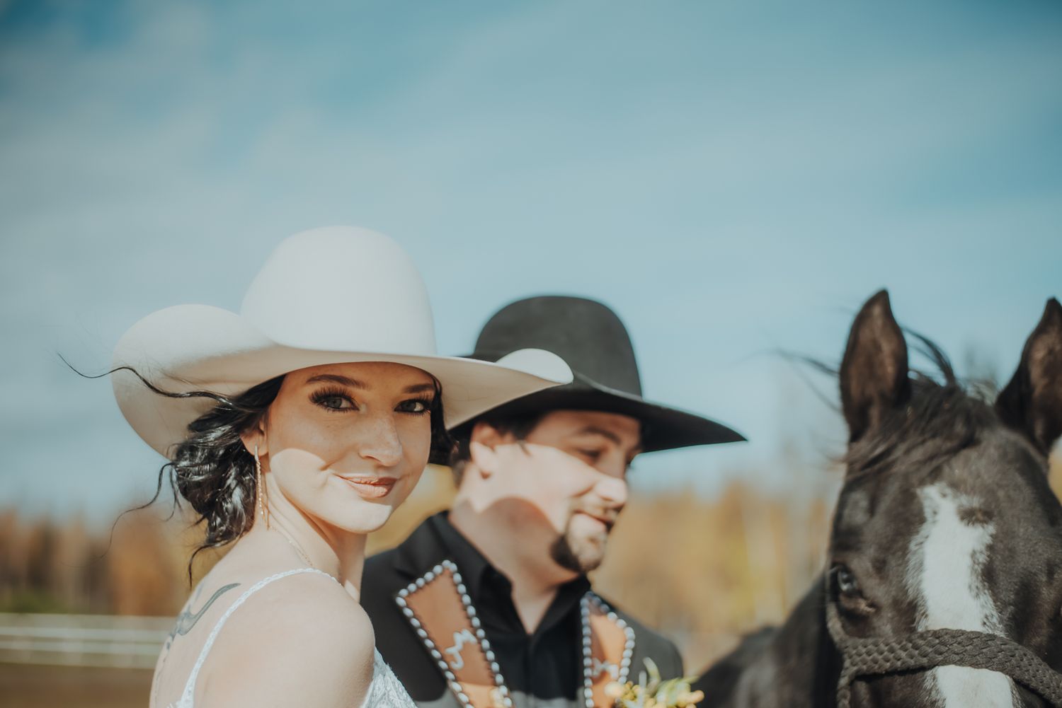 Cowboy couple poses with horses in a rustic outdoor setting.