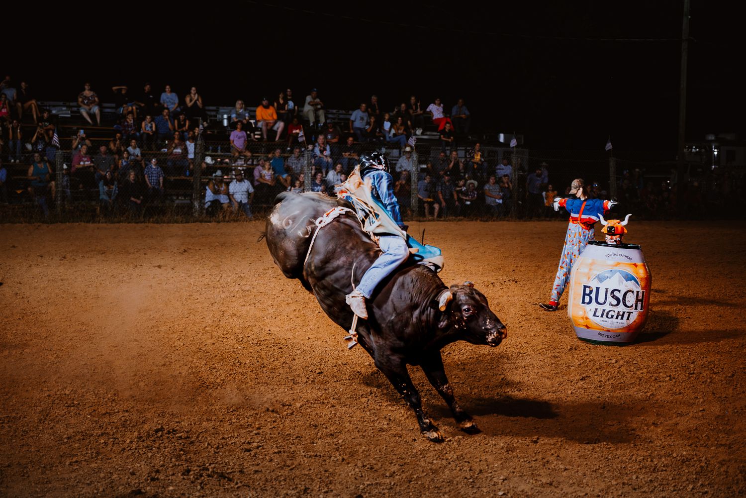 Rodeo rider competes in barrel racing event under stadium lights at night.