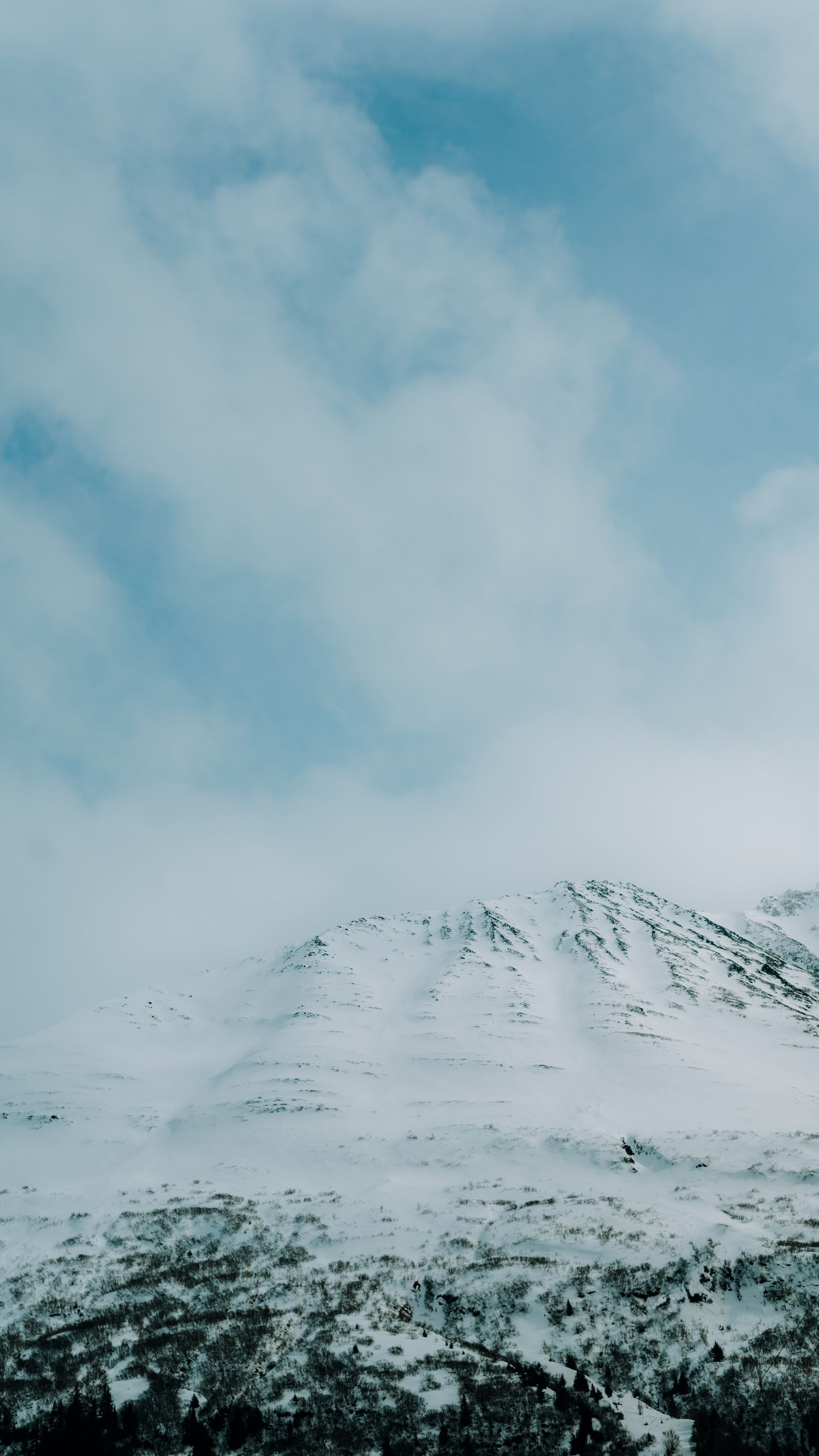 Snow-covered mountain peaks against bright blue sky with wispy clouds.