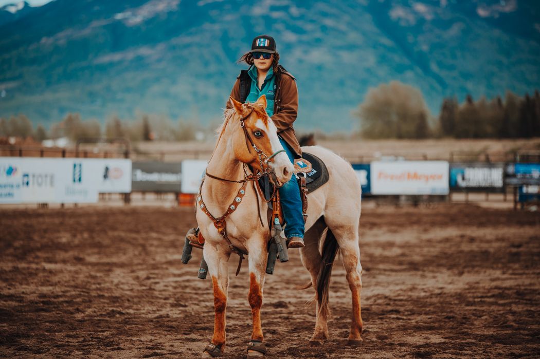 Rider on light-colored horse in western arena with mountains in background.