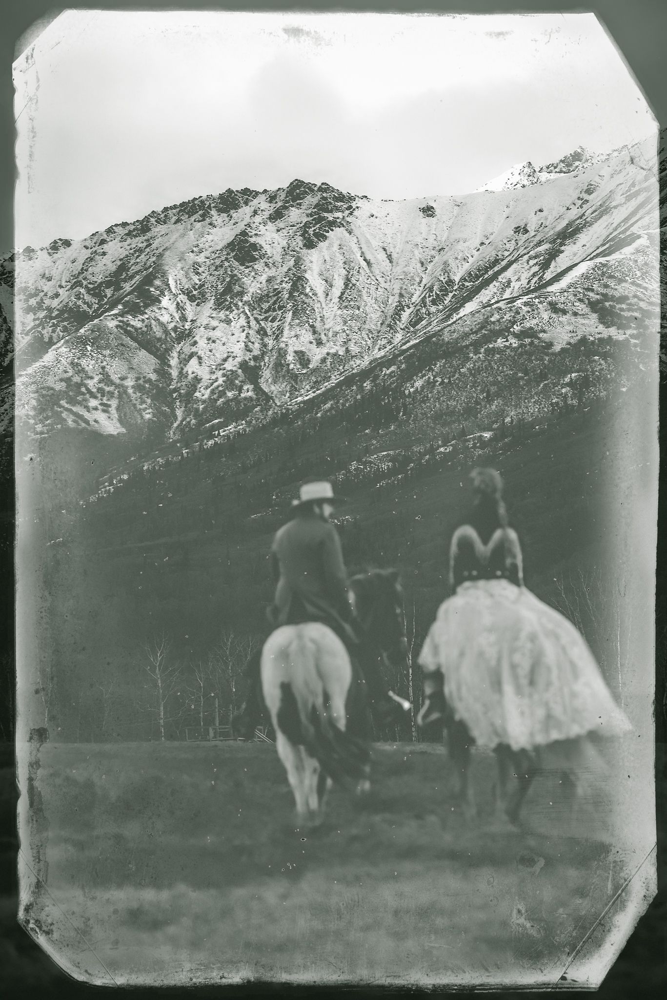 Vintage black and white photograph of horse riders in front of snowy mountain.