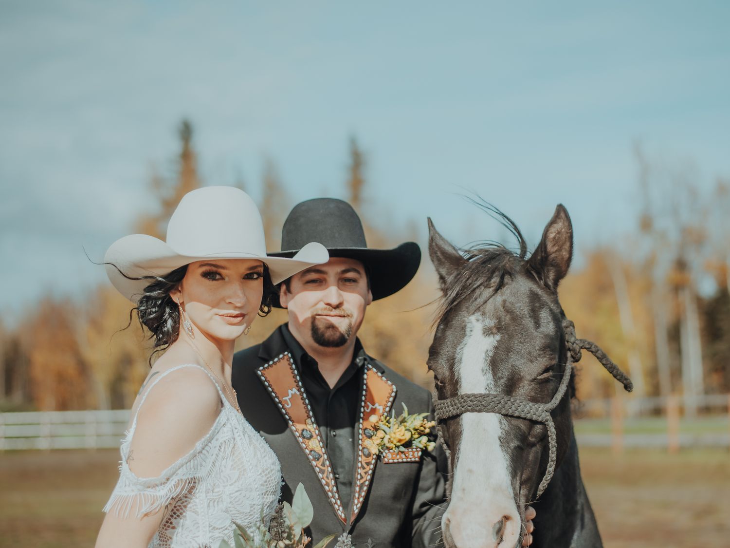 Western-styled couple poses with their horse in an autumn field.
