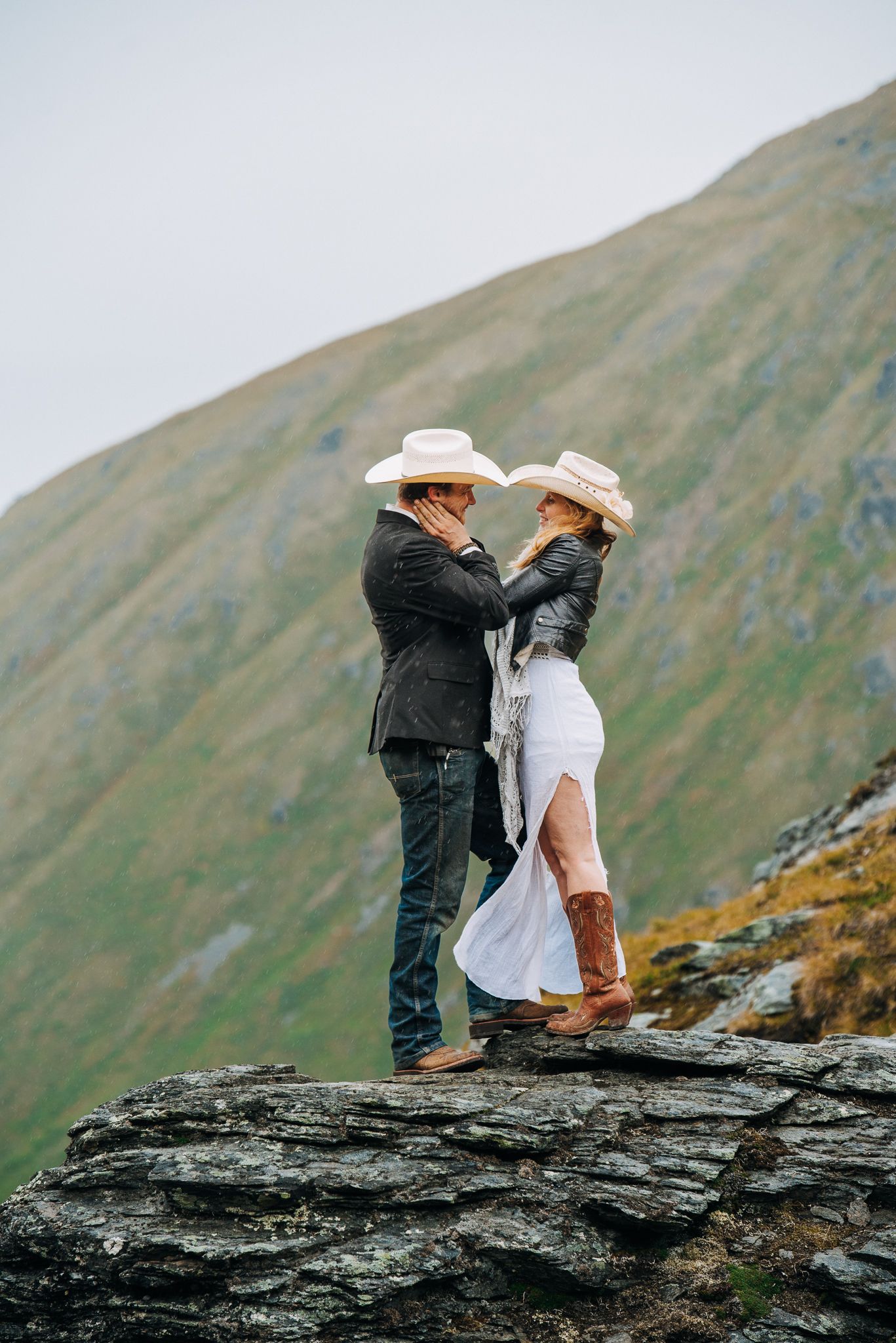 Couple in western attire standing on rocky mountain overlook.