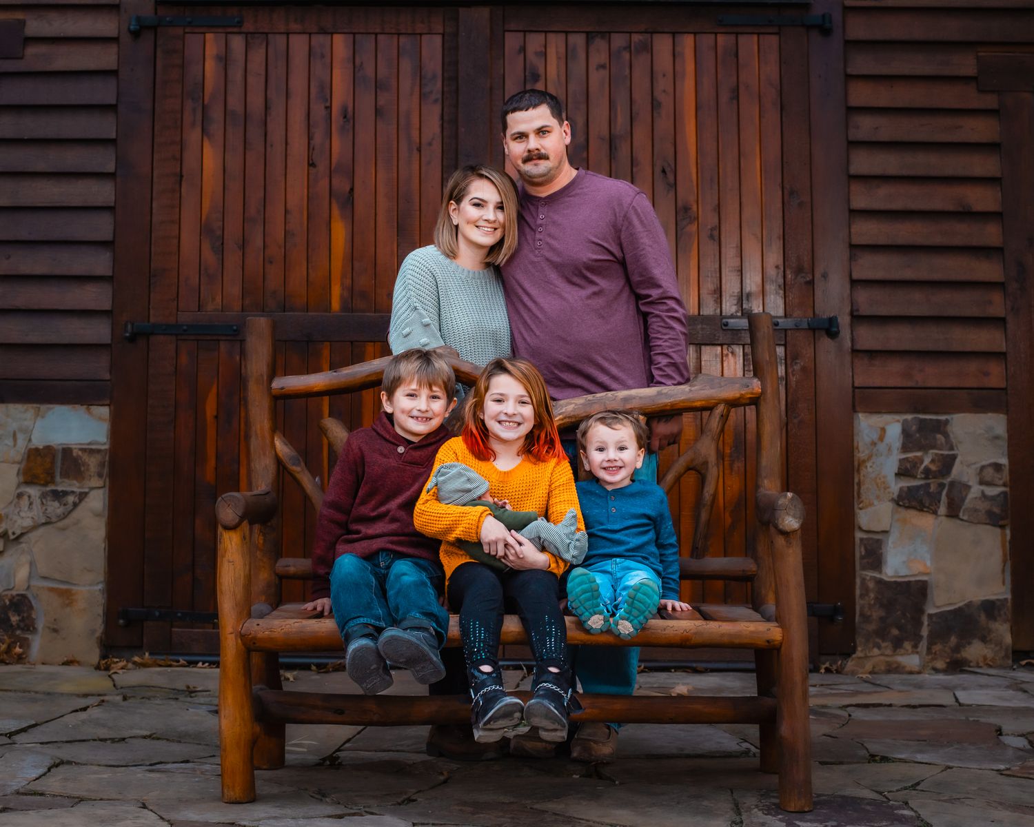 Happy family group portrait on a wooden bench against rustic barn doors.