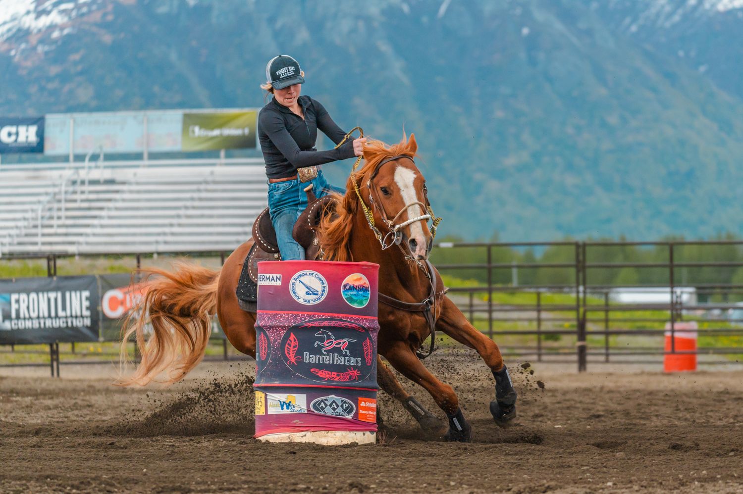 Barrel racing competition with horse and rider against mountain backdrop.