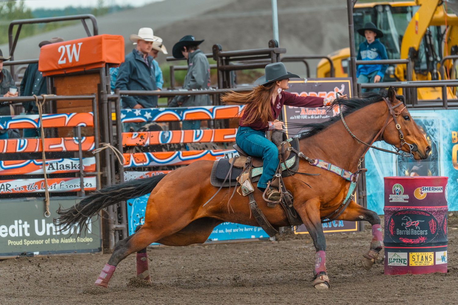 Barrel racing action shot with rider guiding horse around pink barrel in rodeo arena.