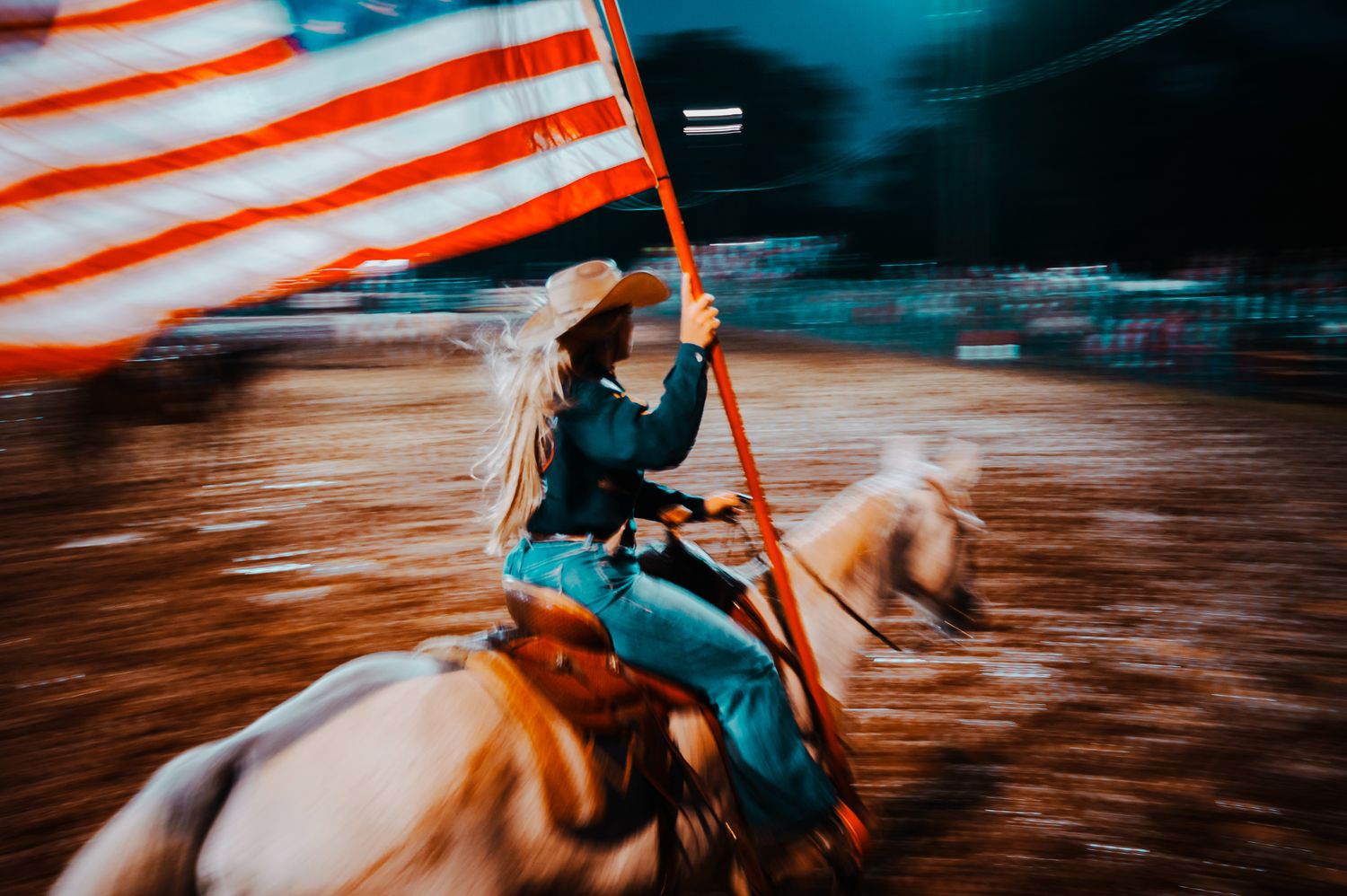 American flag waves dramatically during nighttime rodeo competition.