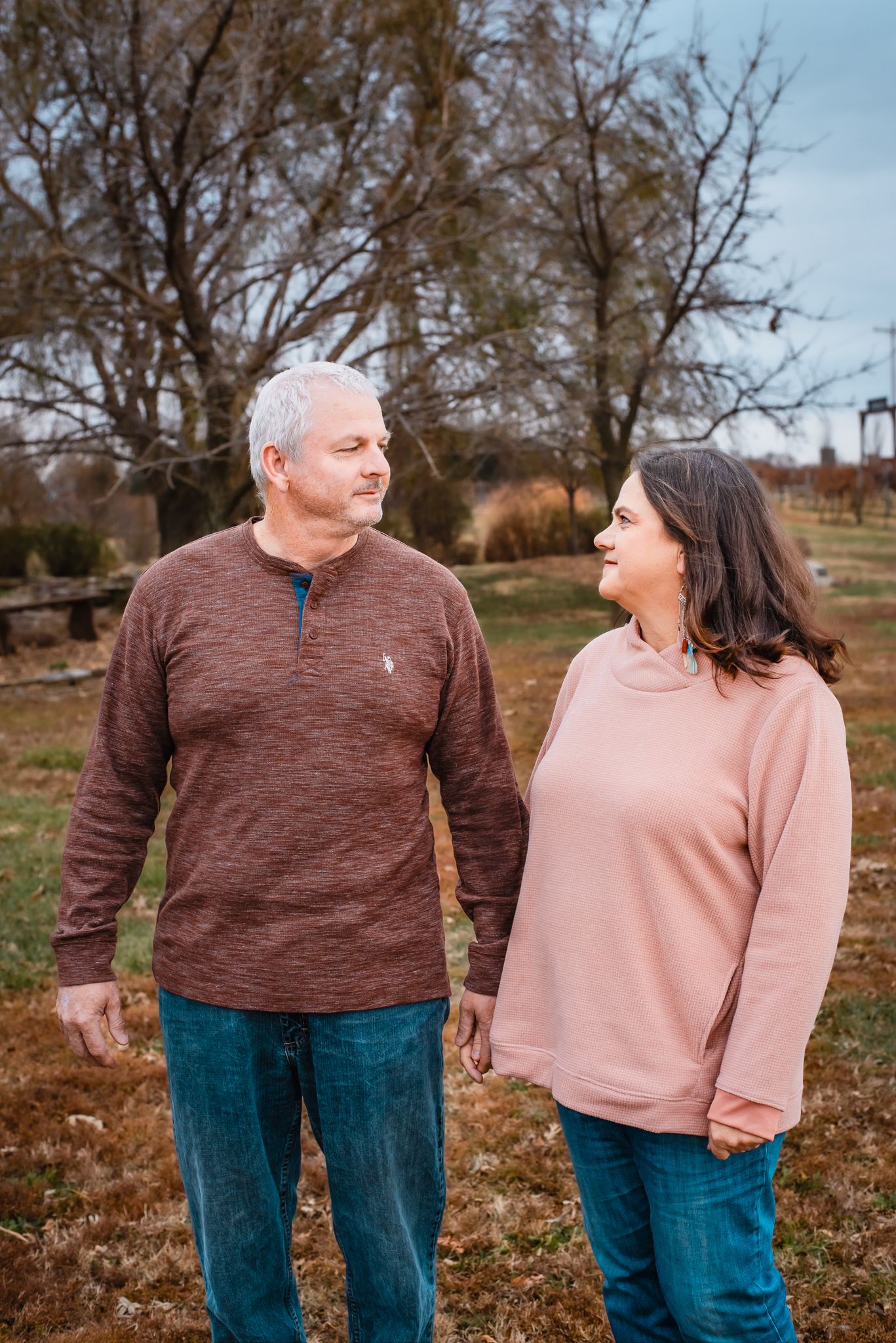 Couple in casual sweaters walking together through fallen autumn leaves.