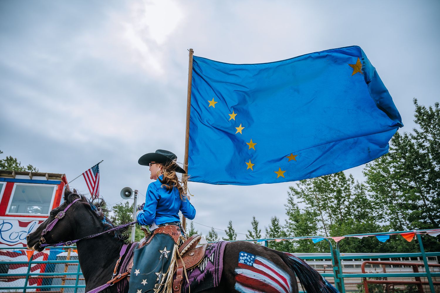 Rider carrying European Union flag on horseback at rodeo event with cloudy sky backdrop.