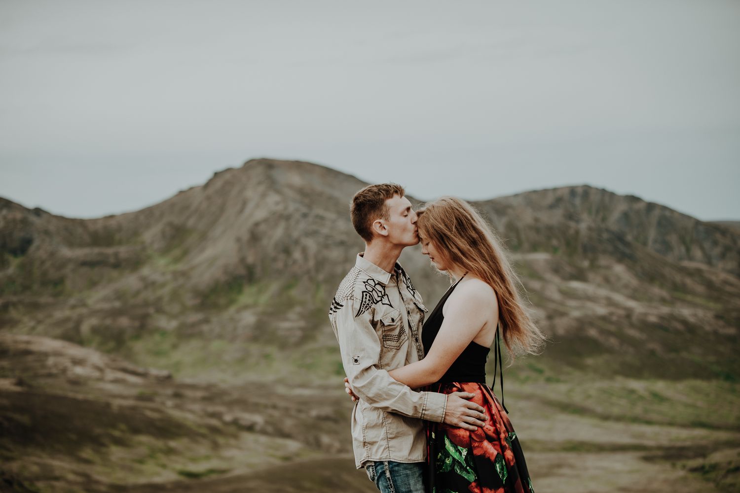 Intimate couple embracing against mountain landscape backdrop.