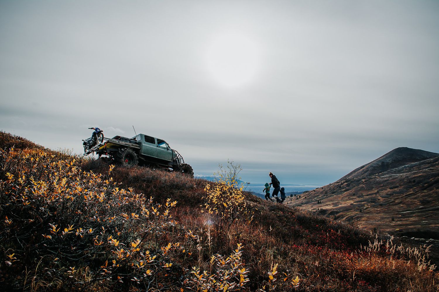 A dramatic mountain landscape with a vehicle silhouetted against an overcast sky.