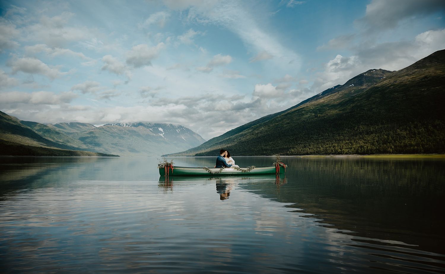 Serene mountain lake landscape with calm waters reflecting cloudy skies.