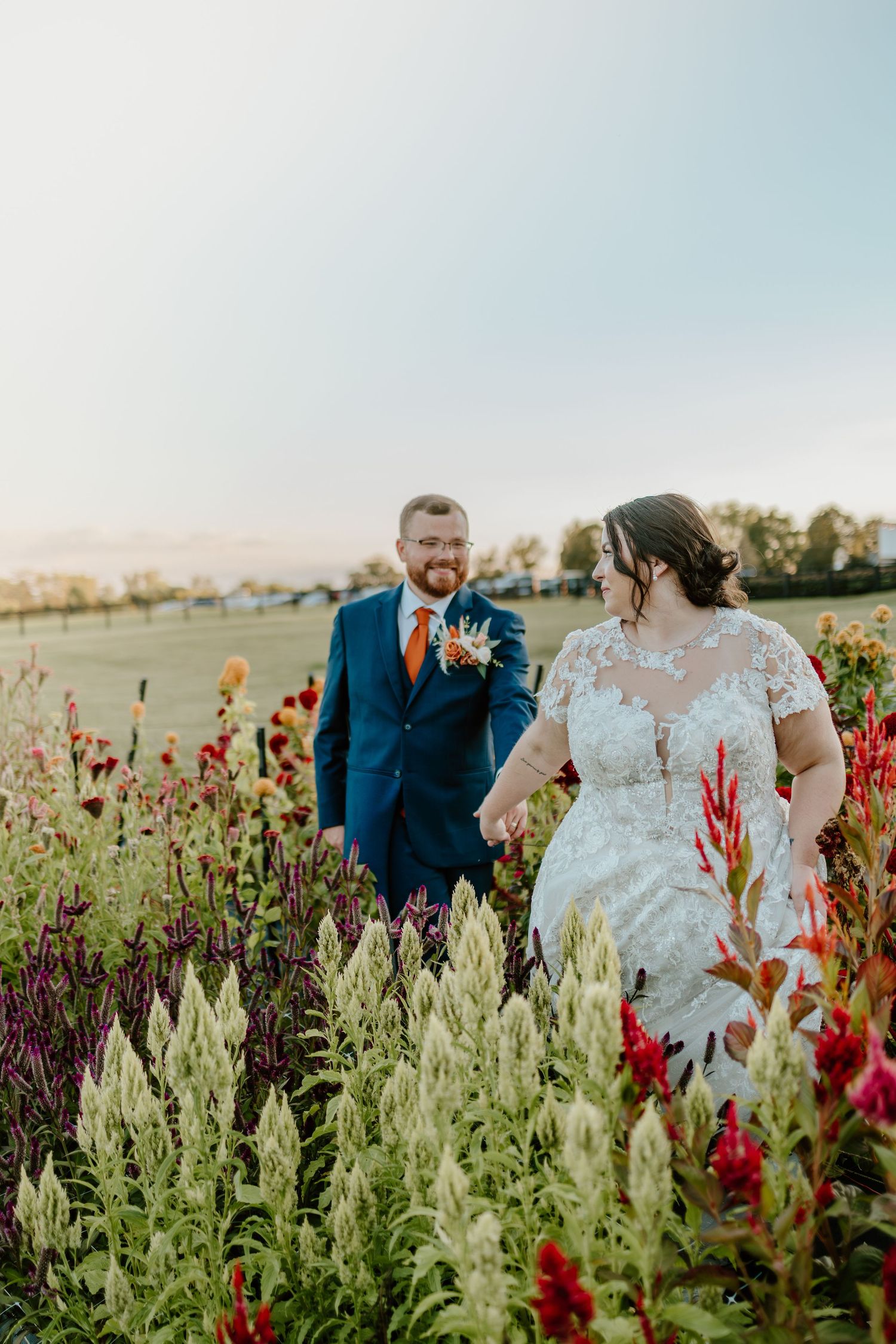 A couple stands together in a field of vibrant red wildflowers and sage green plants on a sunny day.