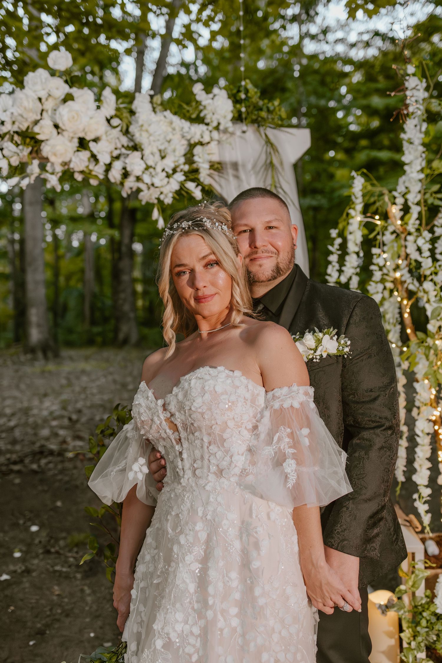 A romantic outdoor wedding photo shoot with string lights and floral decorations in a wooded setting.