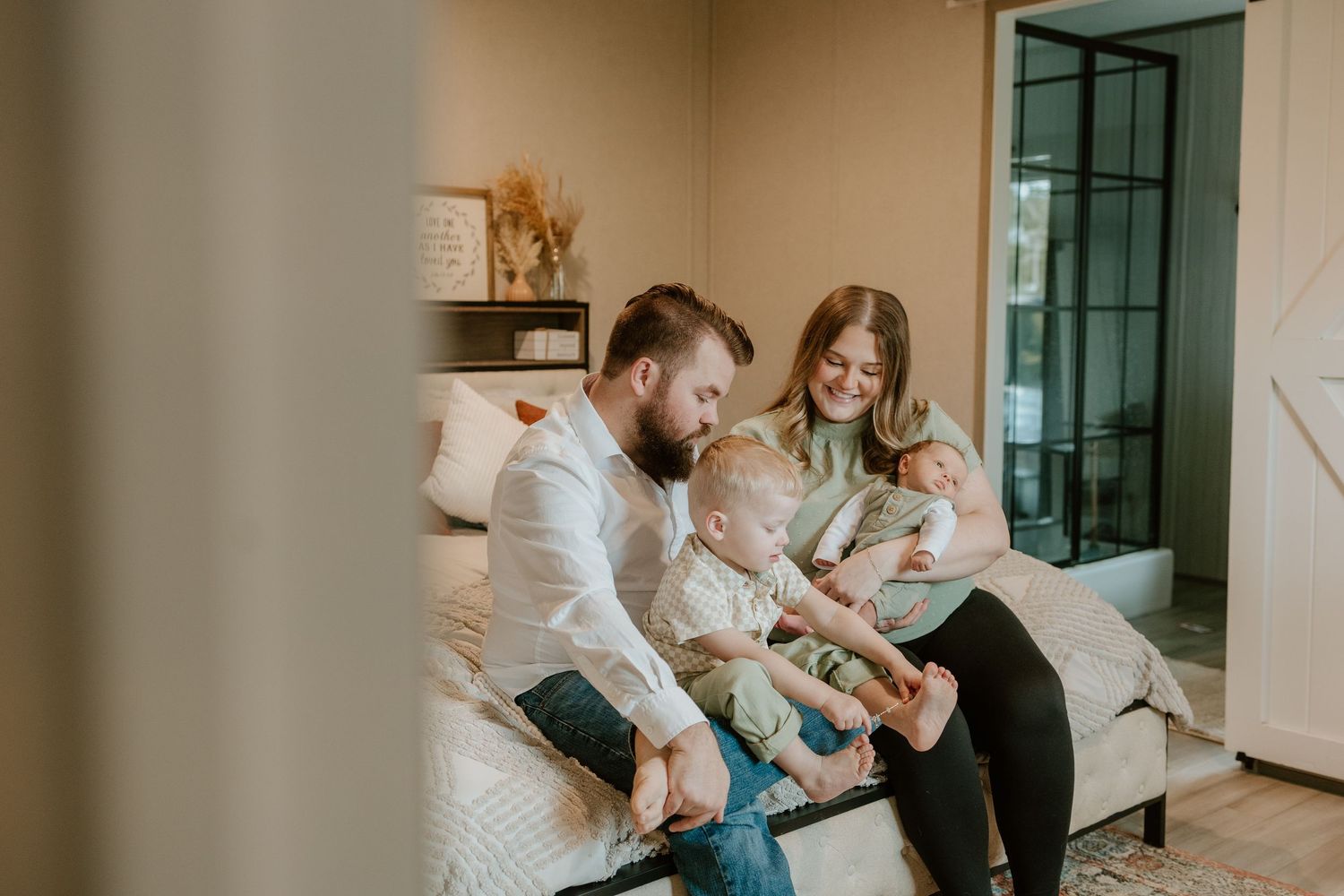 Family sits together on white couch in cozy living room with modern decor and natural lighting.