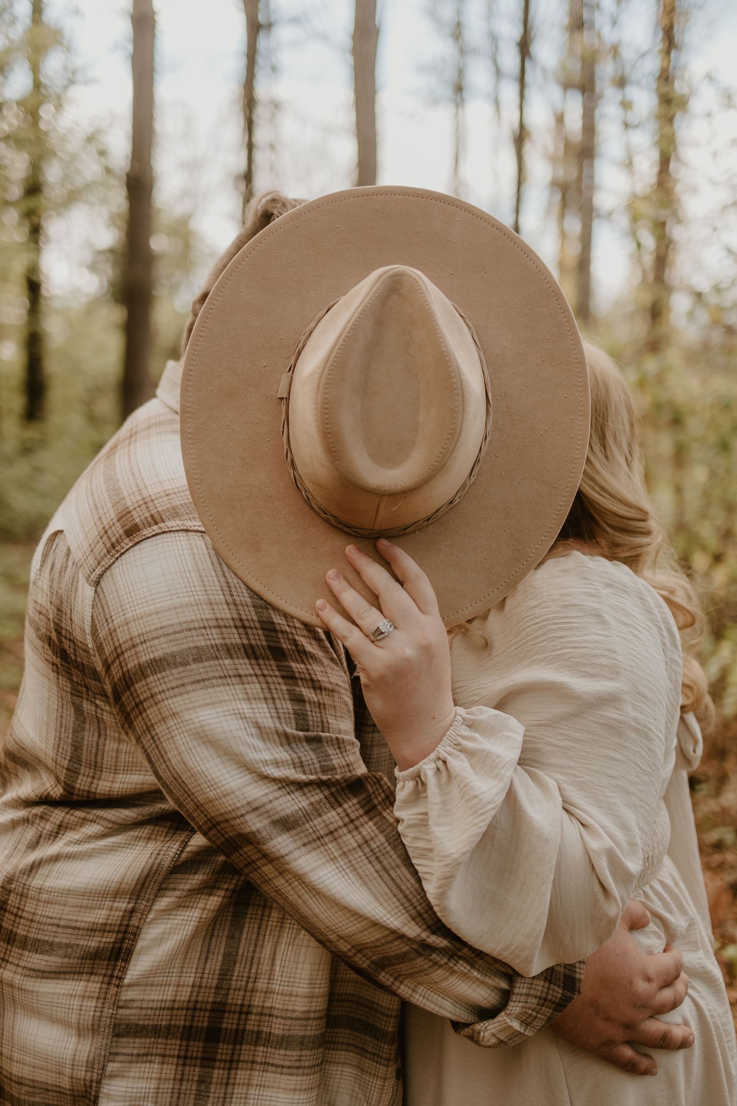 A couple shares intimate moments while wearing a brown hat against a forest backdrop.
