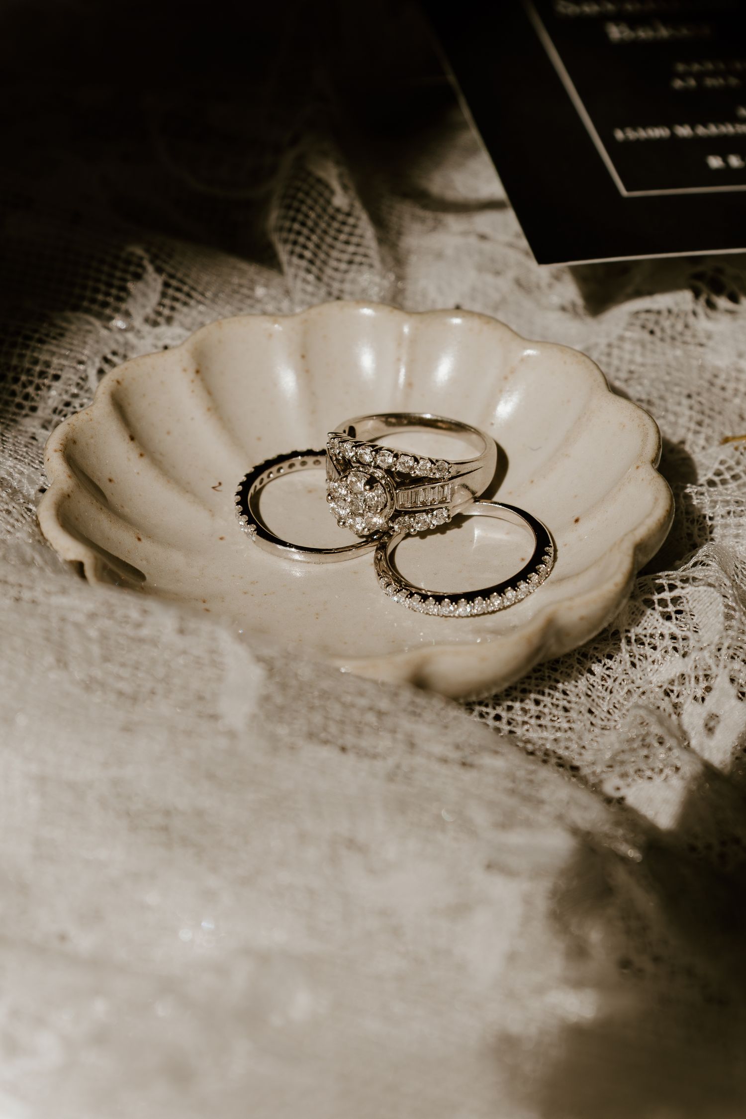 A vintage-style sepia photograph shows a delicate shell-shaped dish with a ring placed on lace fabric.