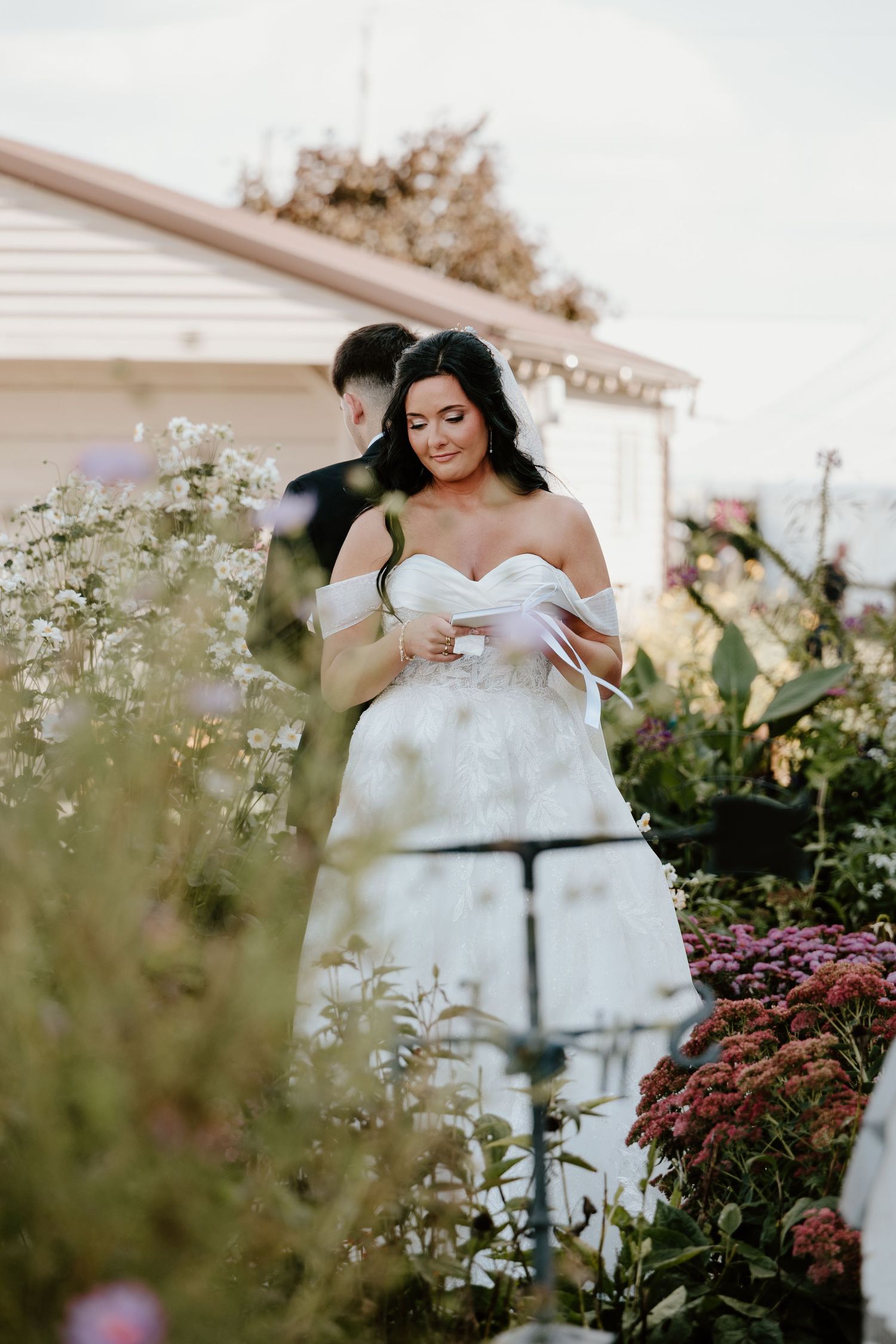 A romantic garden wedding scene with a bride in a white off-shoulder dress surrounded by delicate wildflowers and greenery.