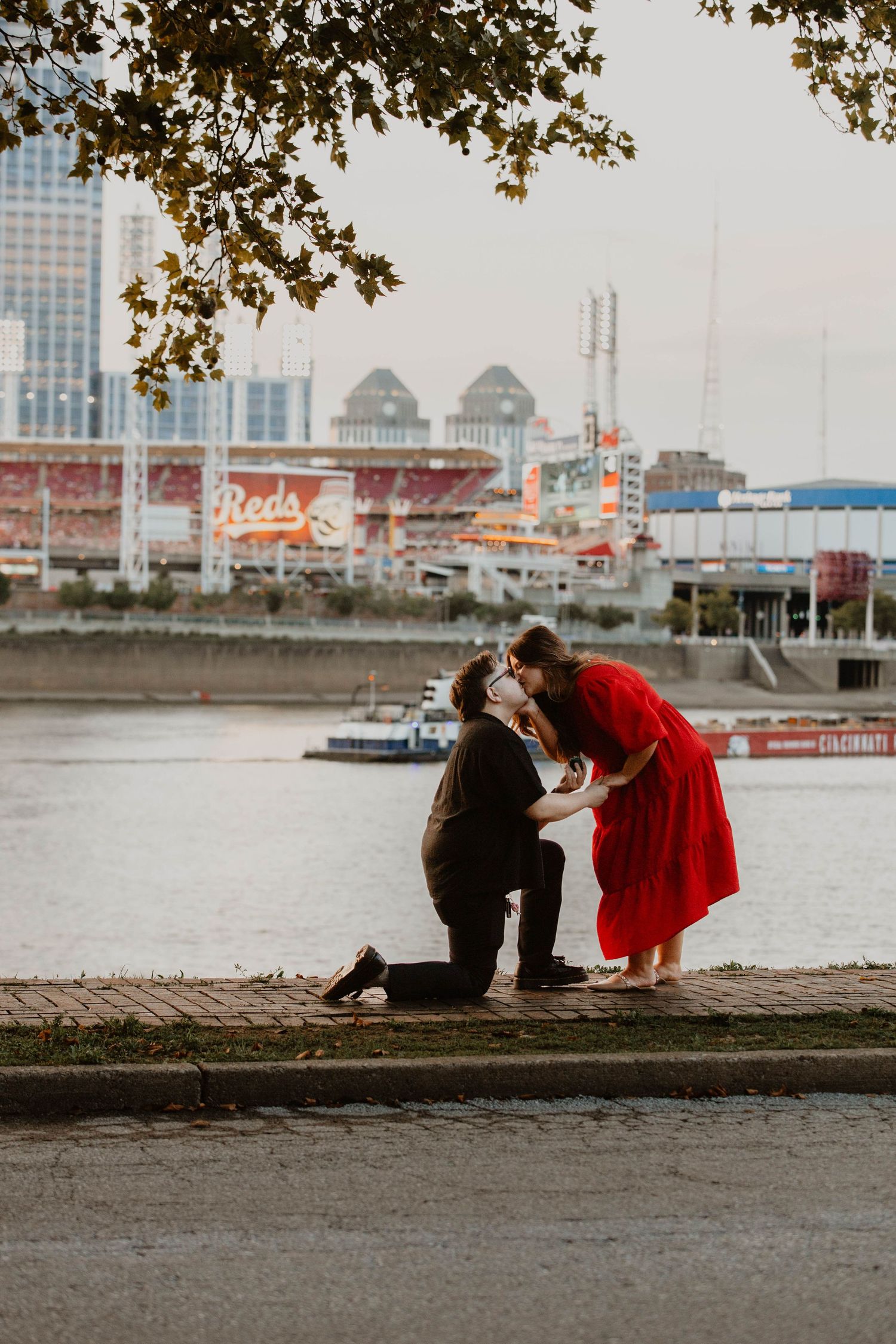 A proposal scene unfolds along a waterfront with city buildings in the background.