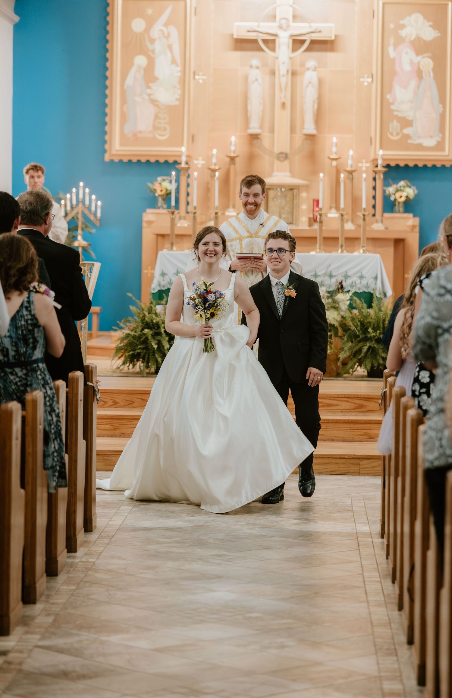 A panoramic view of a wedding ceremony in a church with blue walls and ornate decorations along the aisle.