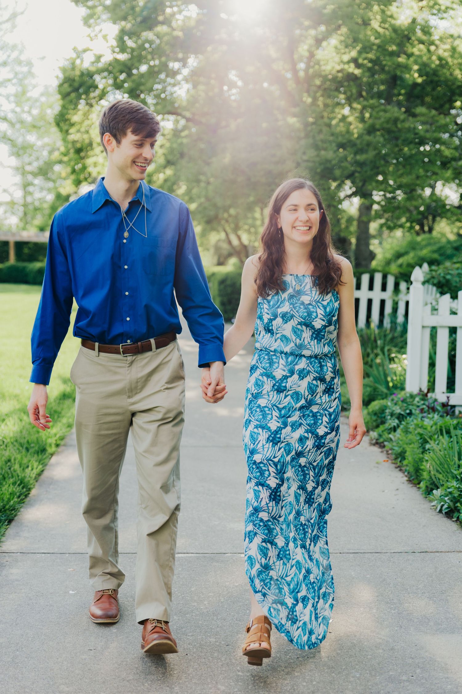 A couple walking hand in hand along a garden path wearing coordinated blue and floral outfits.