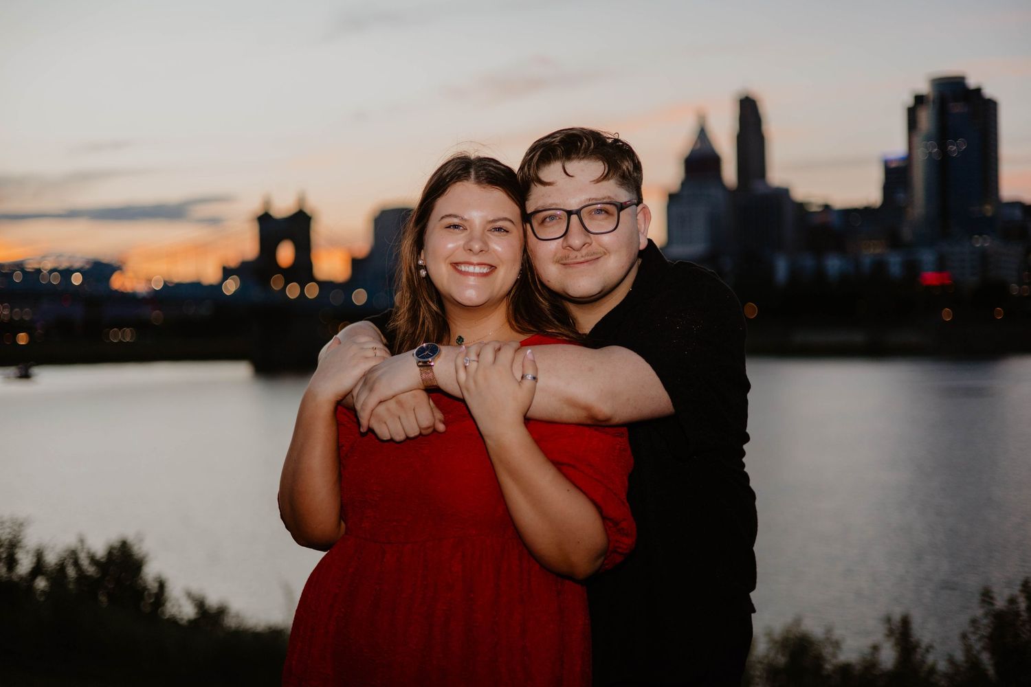 Romantic couple standing together against urban waterfront backdrop during golden hour.