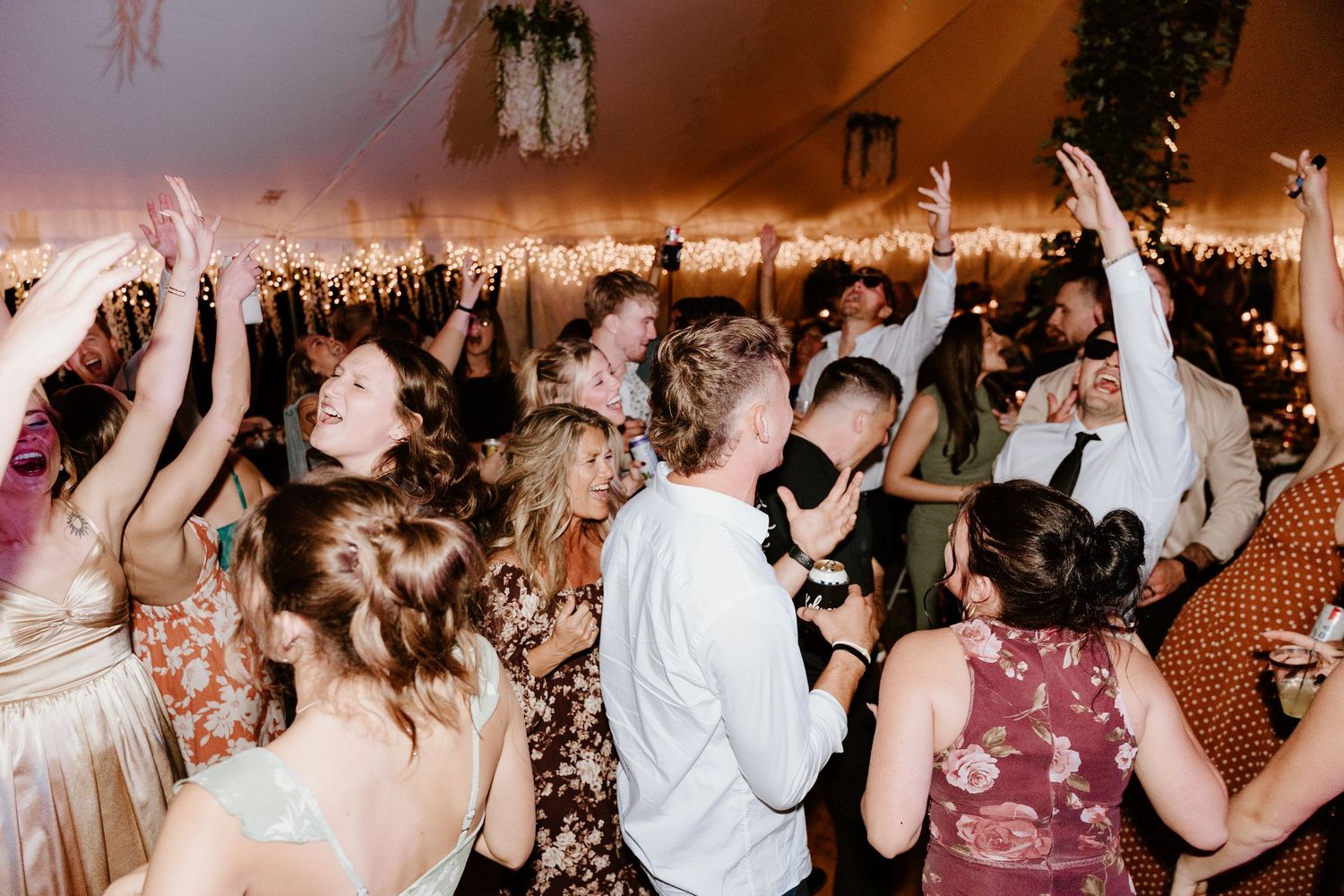 Wedding reception guests dance with hands raised on a crowded dance floor during an energetic celebration.