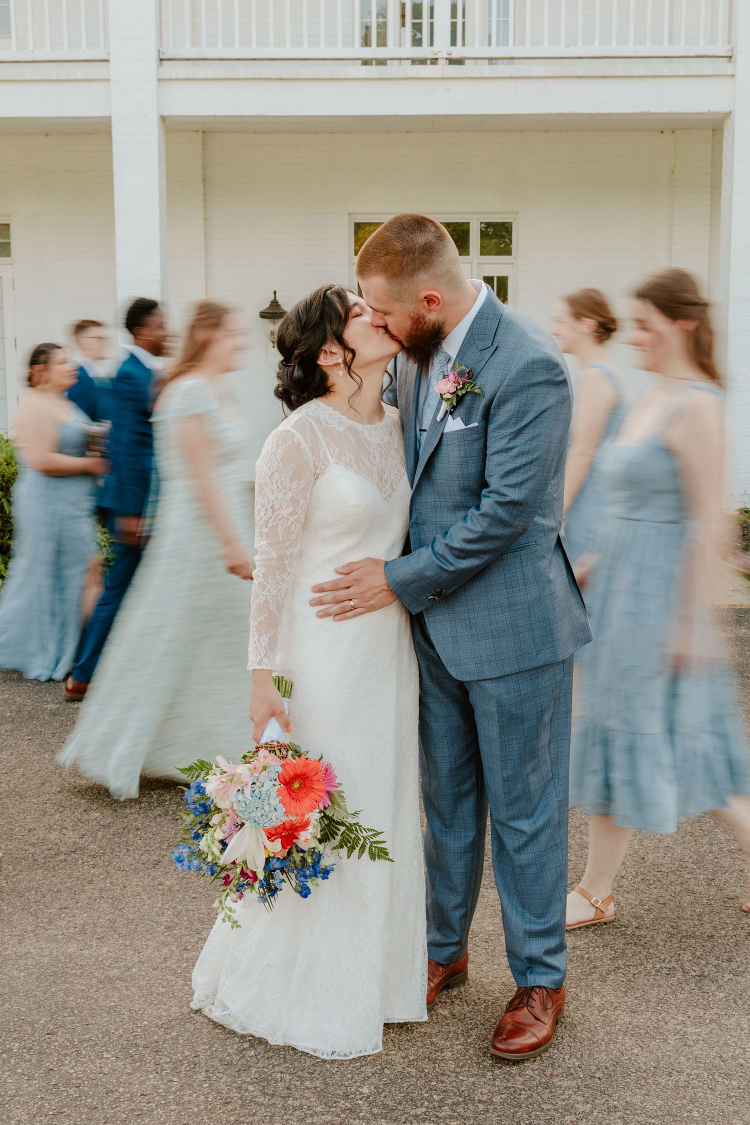 Motion blur captures wedding party dancing and celebrating at outdoor venue with white columns in background.