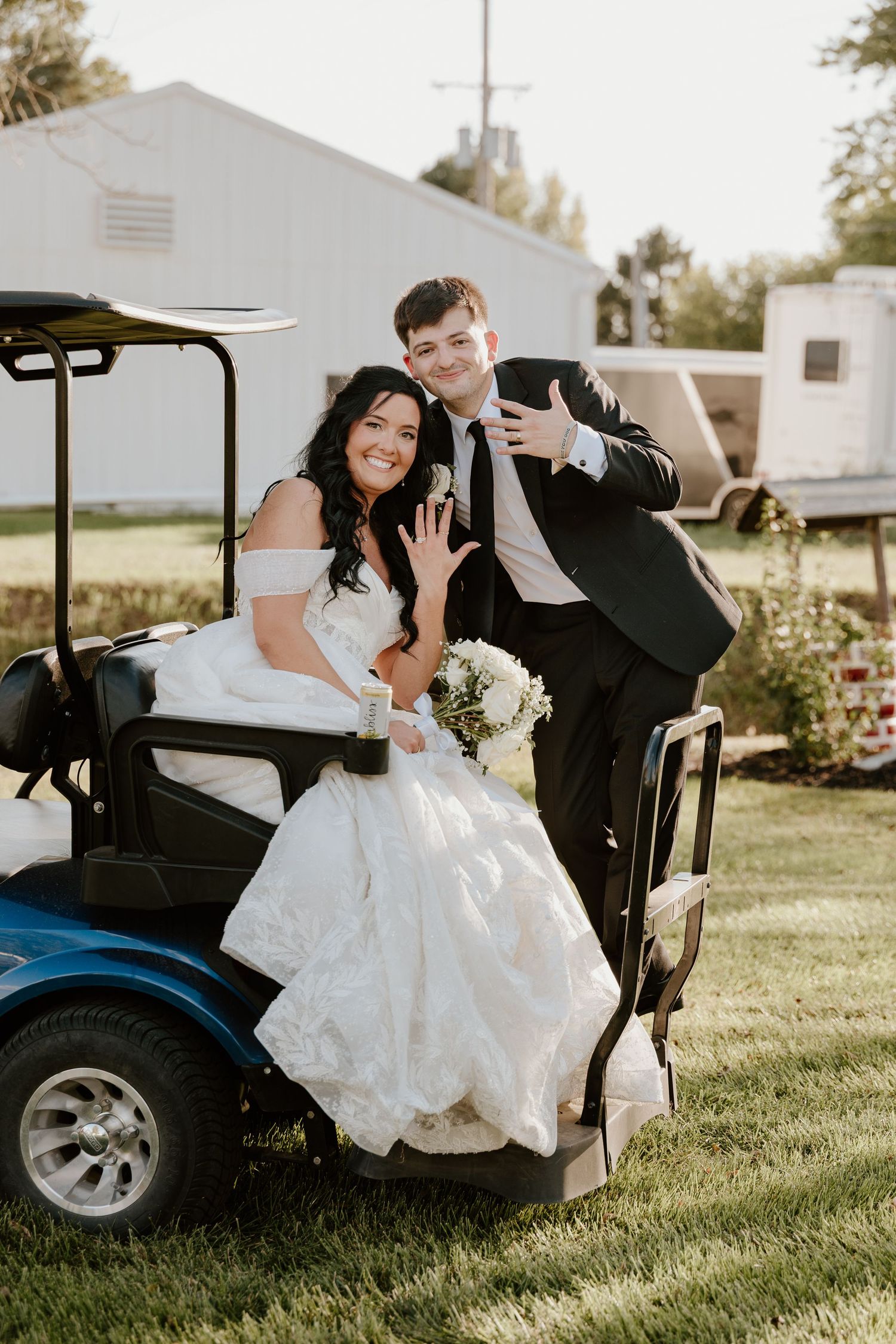 Newlyweds pose together on a golf cart while showing off their rings on their wedding day.