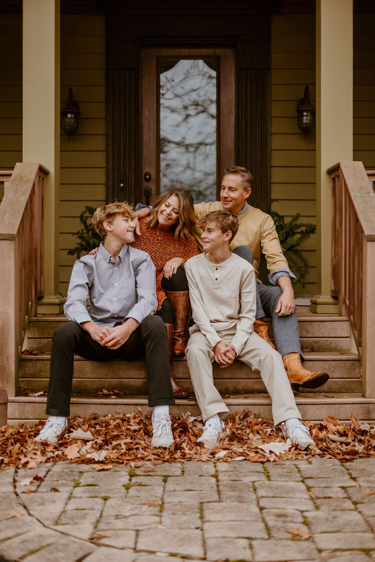 Casual family portrait session on front porch steps with autumn leaves scattered around.