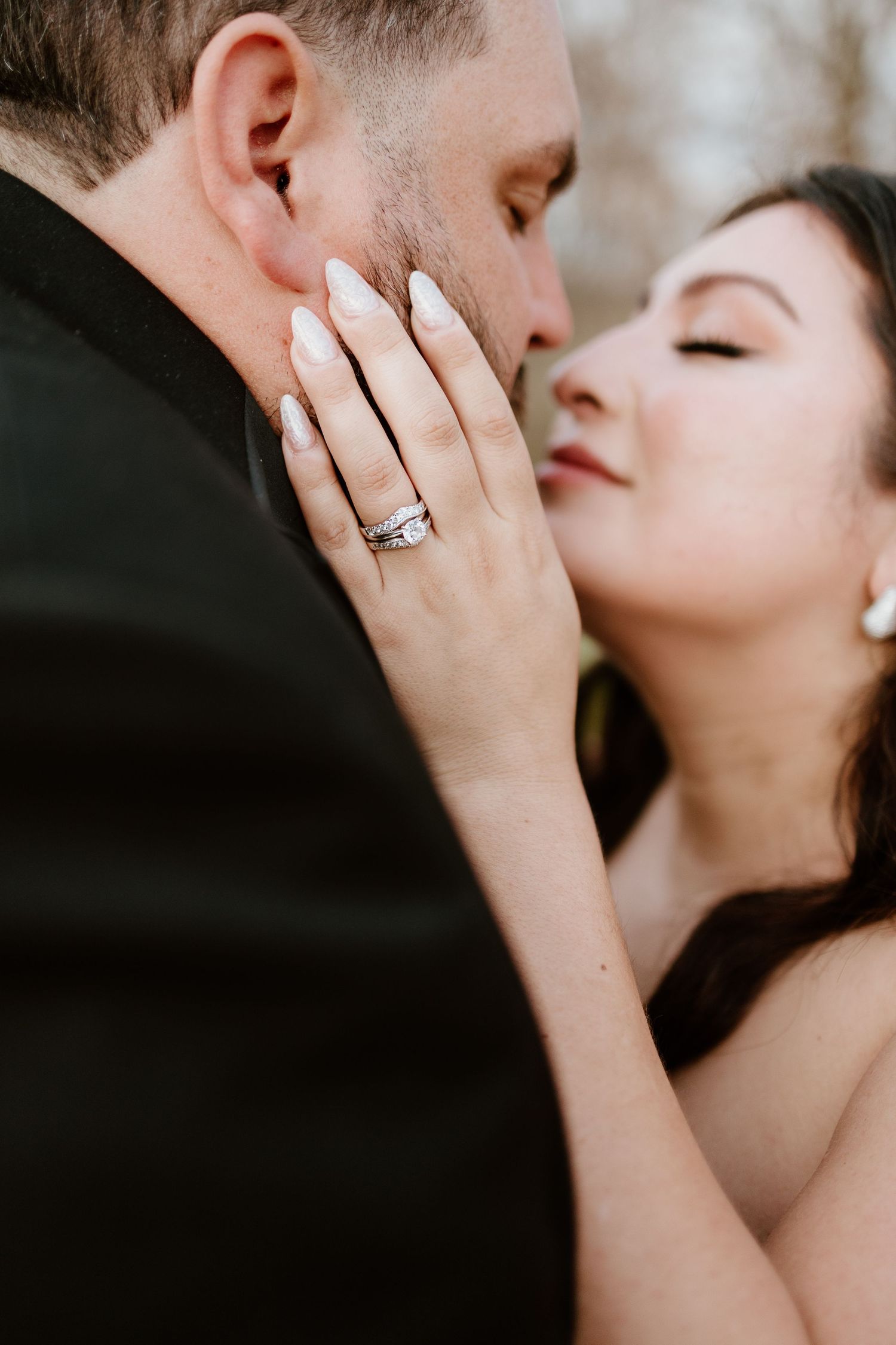 Bride with manicured nails and diamond wedding ring gently touches grooms face in a romantic close-up portrait.