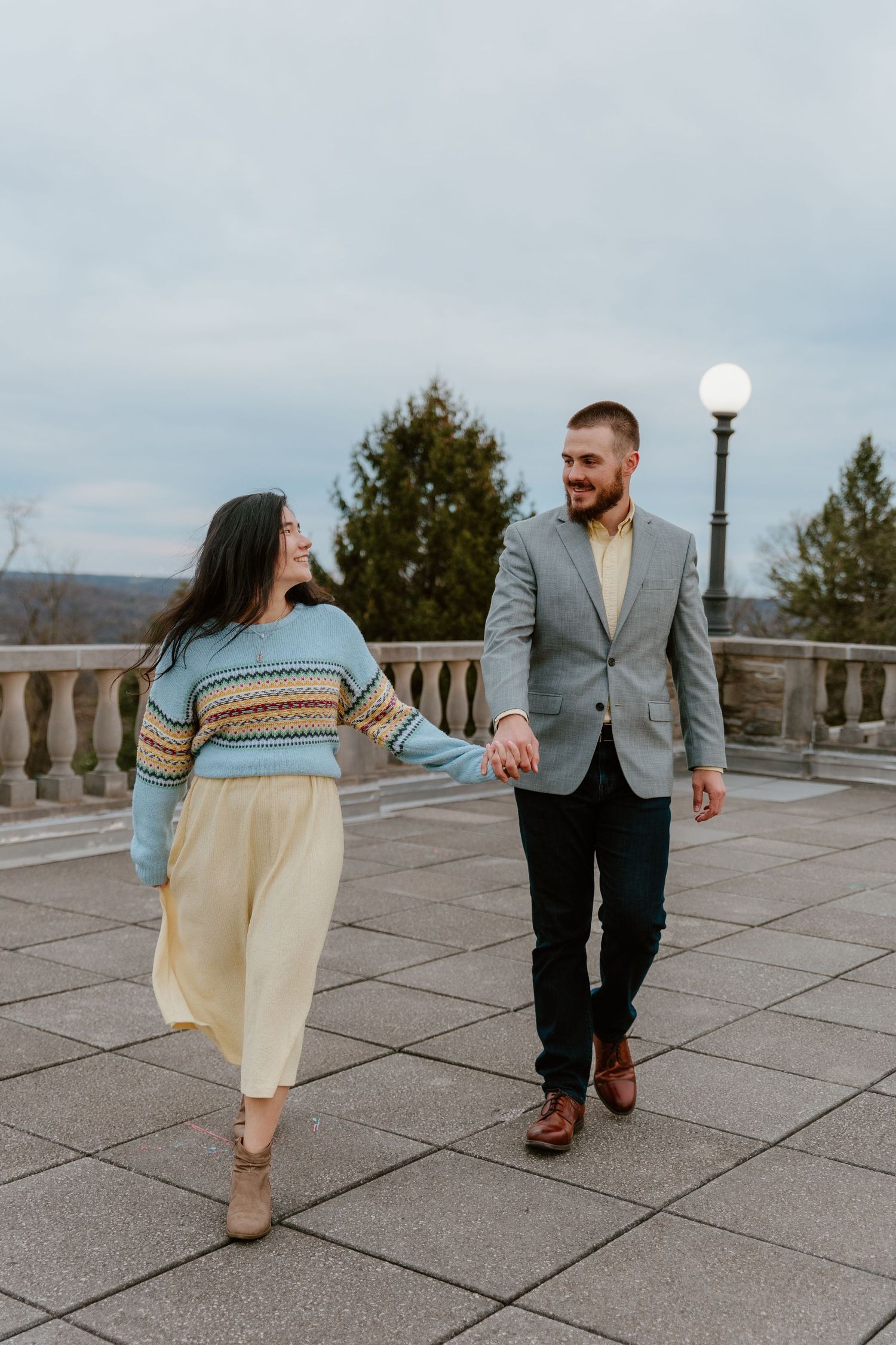 Couple walking together on stone terrace holding hands in casual attire.