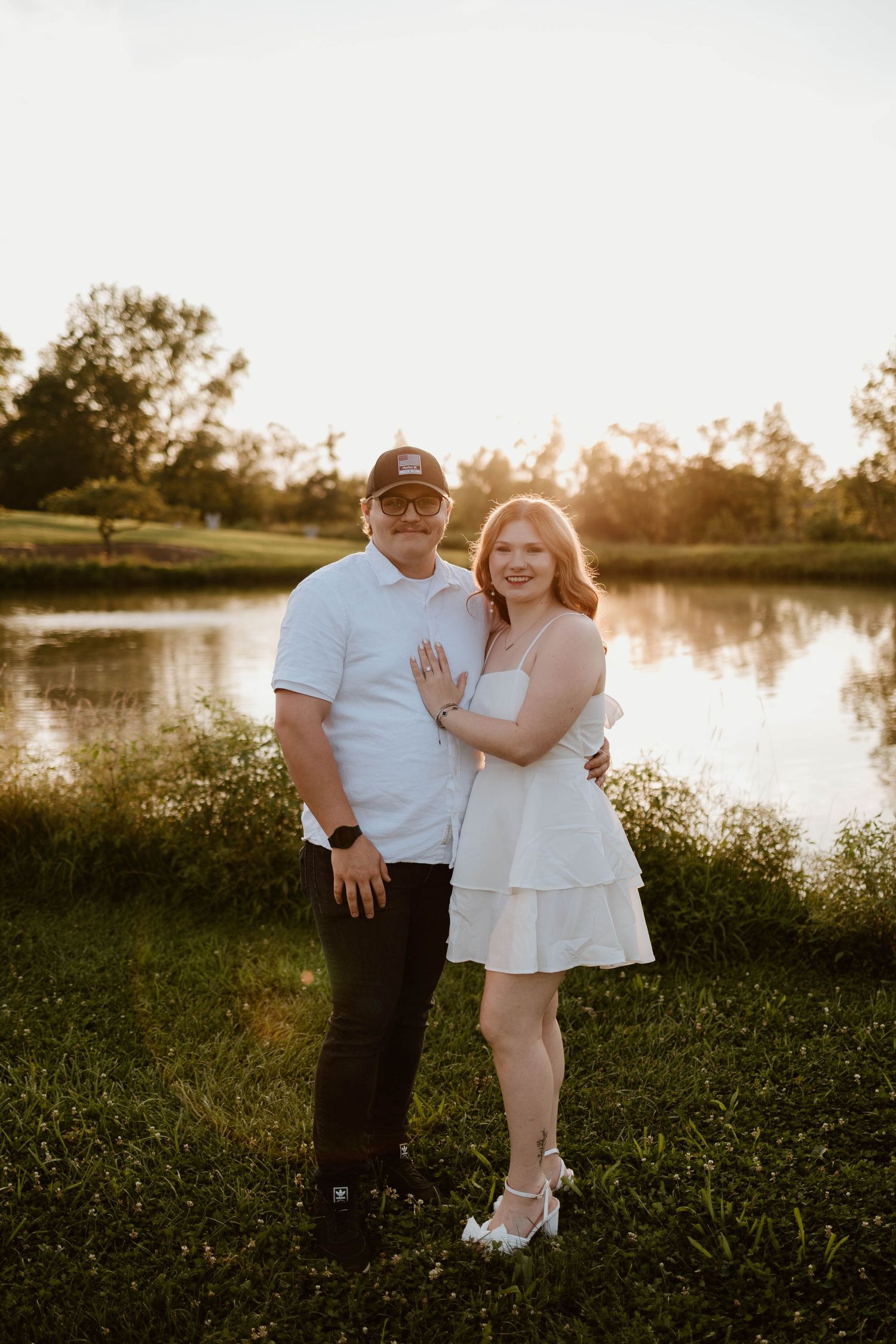 Sunset engagement photo by a serene lake with coordinated white and casual outfits.